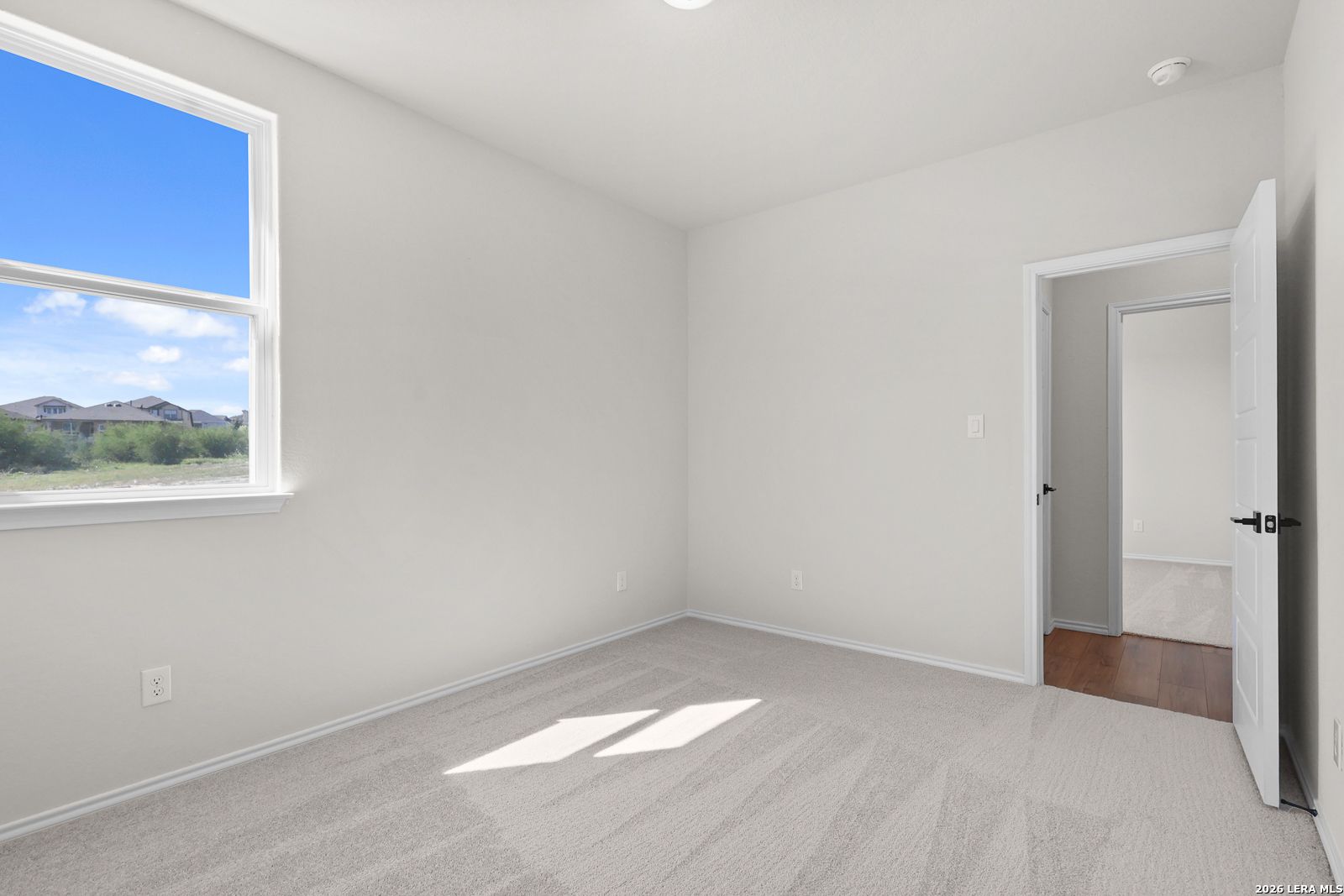Bright empty bedroom with plush carpet, large window, and hardwood hallway in Davidson Homes Glenwood E, San Antonio, TX
