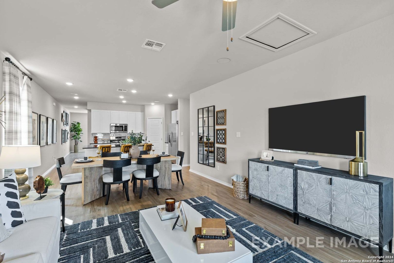Open-concept living and dining area with modern white furniture, TV console, and kitchen island in Davidson Homes The Sabine B, San Antonio
