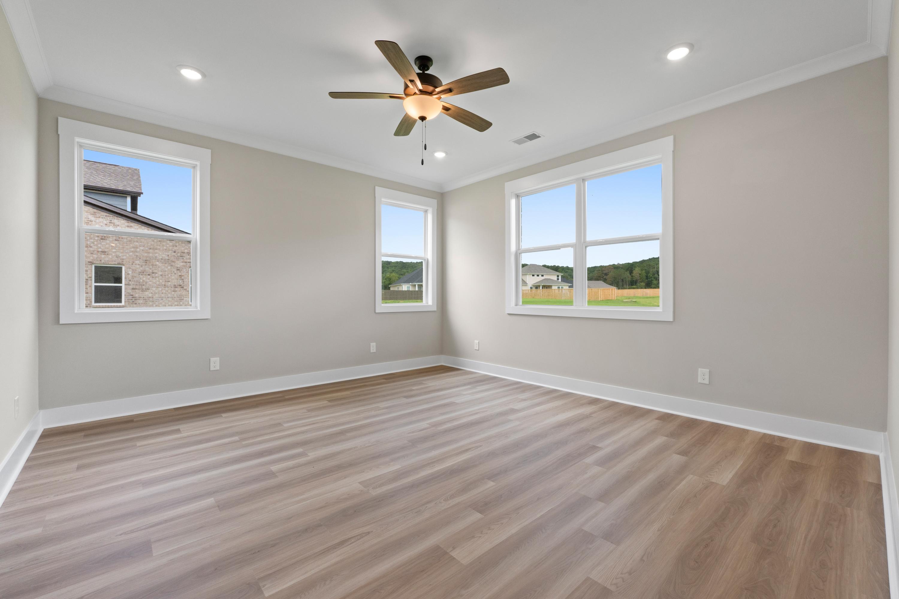 Spacious secondary bedroom in The Oxford B with light hardwood floors, neutral walls, large windows, and ceiling fan