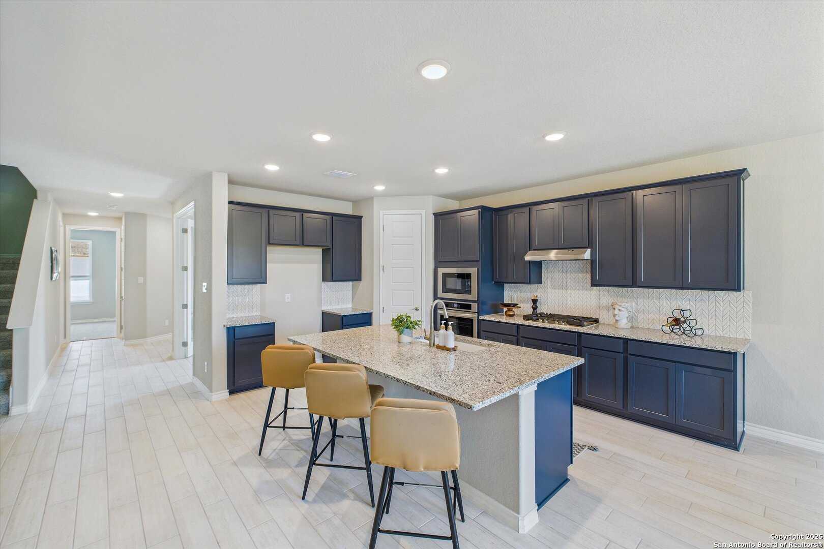 Open-concept kitchen with navy cabinets, quartz island, stainless appliances in The Jennings H by Davidson Homes, Ladera, San Antonio