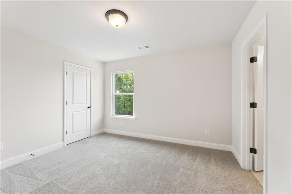 Spacious secondary bedroom with neutral walls, plush gray carpet, and window overlooking greenery in The Hickory B, Buford, Georgia