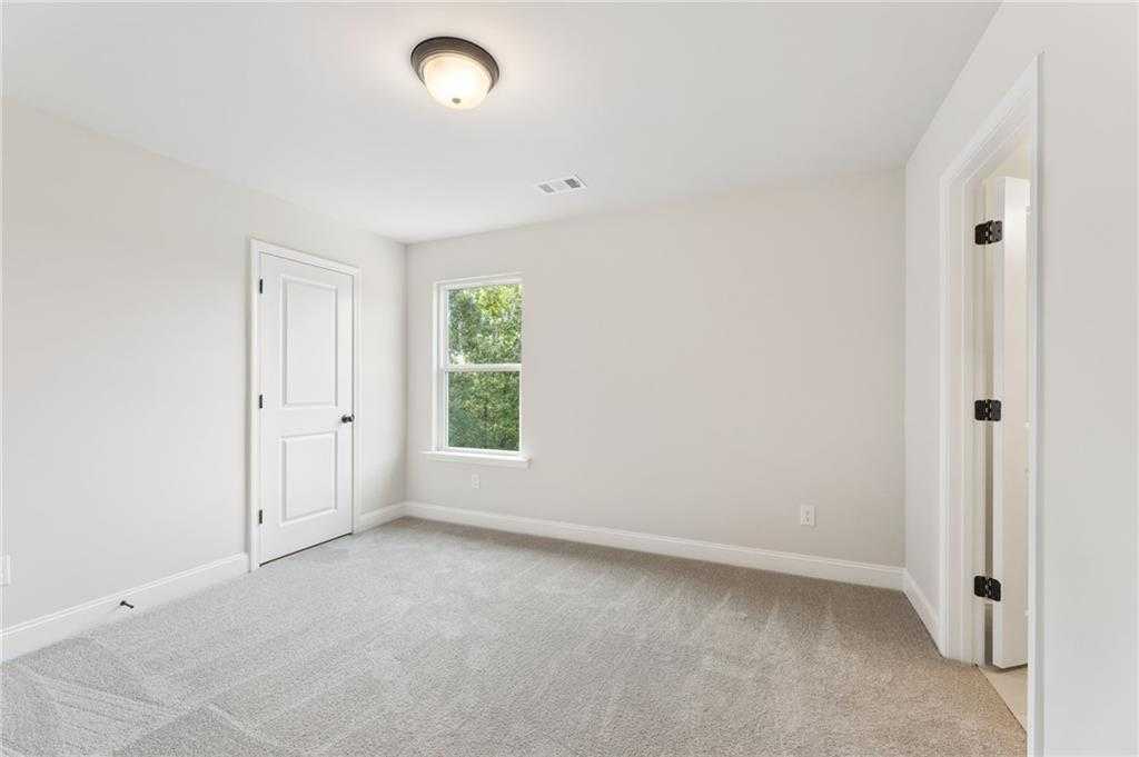 Spacious secondary bedroom with neutral walls, plush gray carpet, and window overlooking greenery in The Hickory B, Buford, Georgia