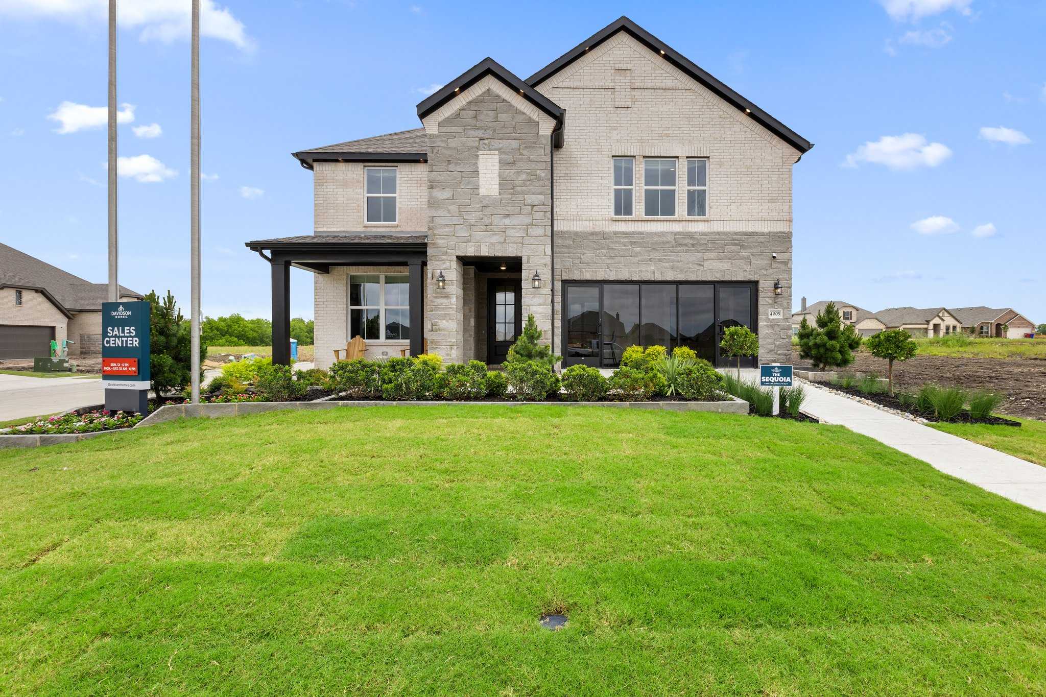 Modern stone-accented home exterior at Mercer Meadows in Royse City TX with covered porch and sales sign by Davidson Homes