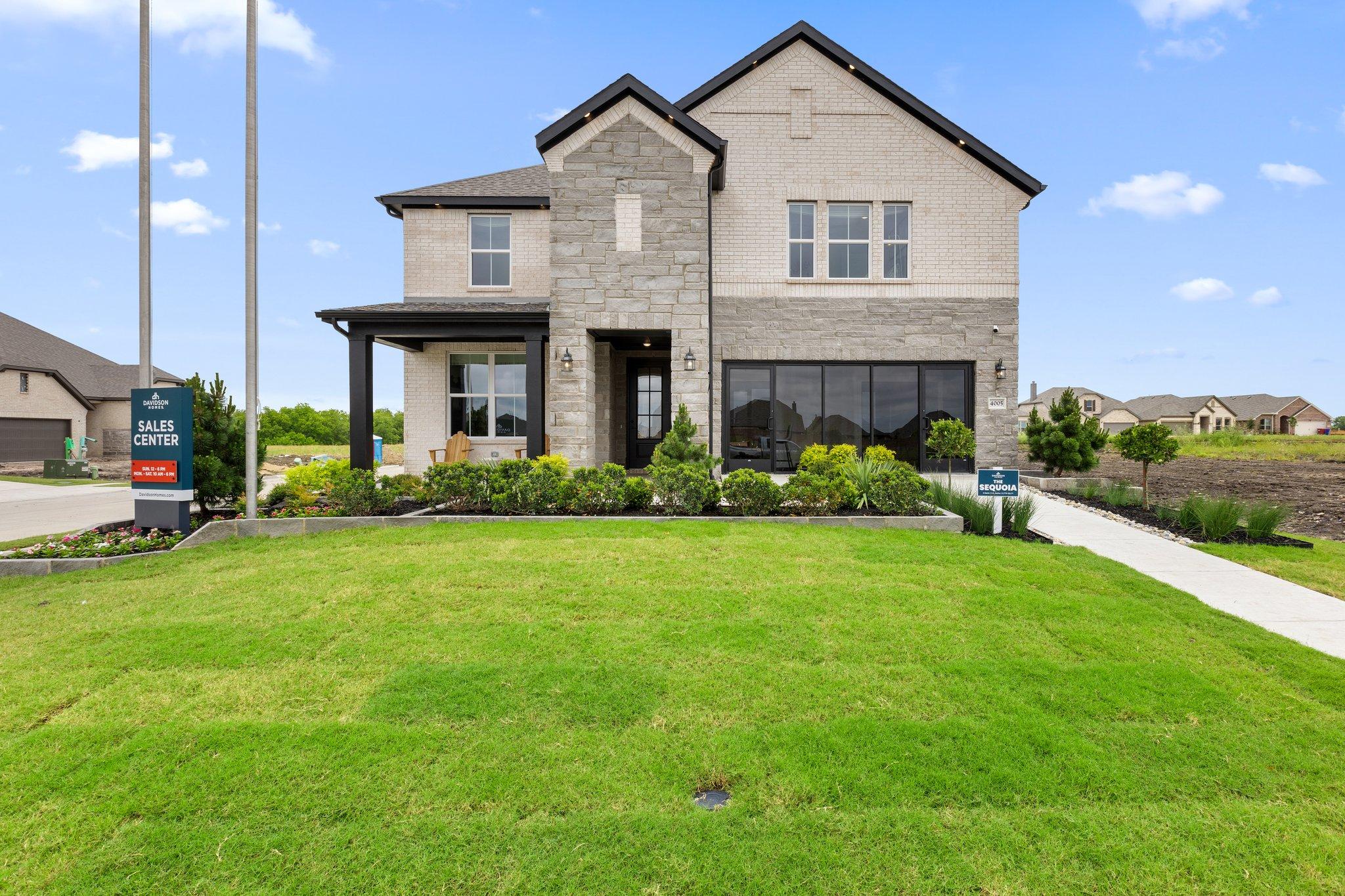 Modern stone-accented home exterior at Mercer Meadows in Royse City TX with covered porch and sales sign by Davidson Homes
