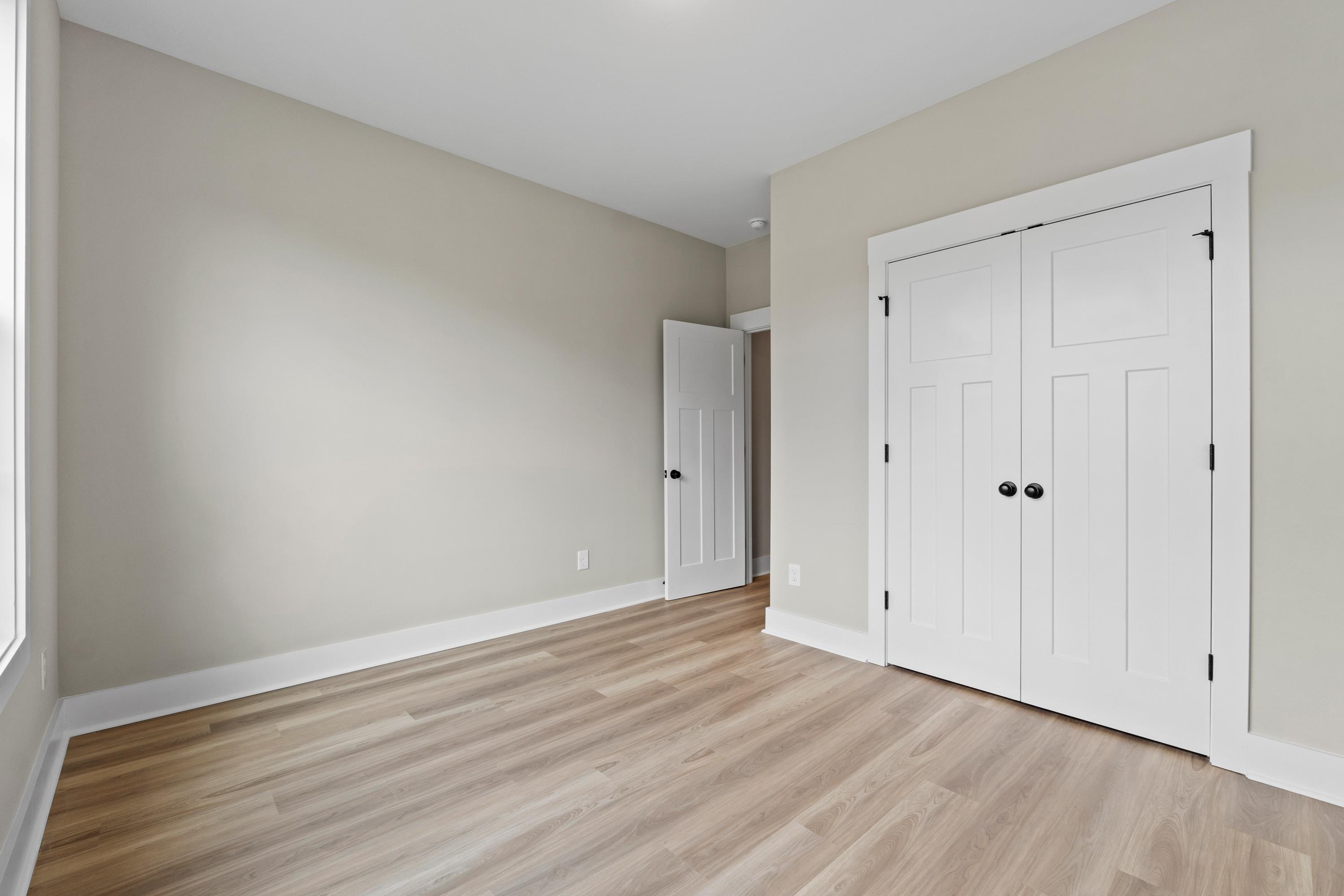 Spacious bedroom in The Oxford by Evermore Homes featuring light oak floors, beige walls, white double closet doors