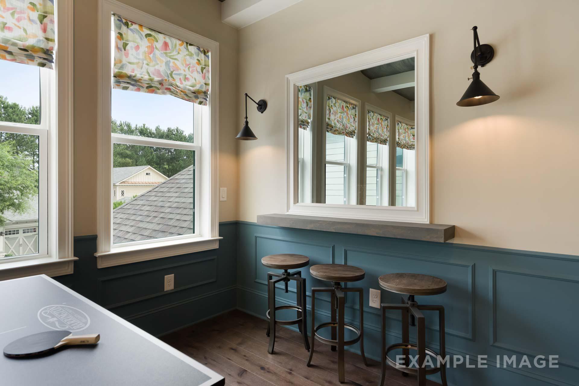 Cozy bar nook in The Seaside C home with wooden stools, large mirror, foosball table, and window views of wooded landscape