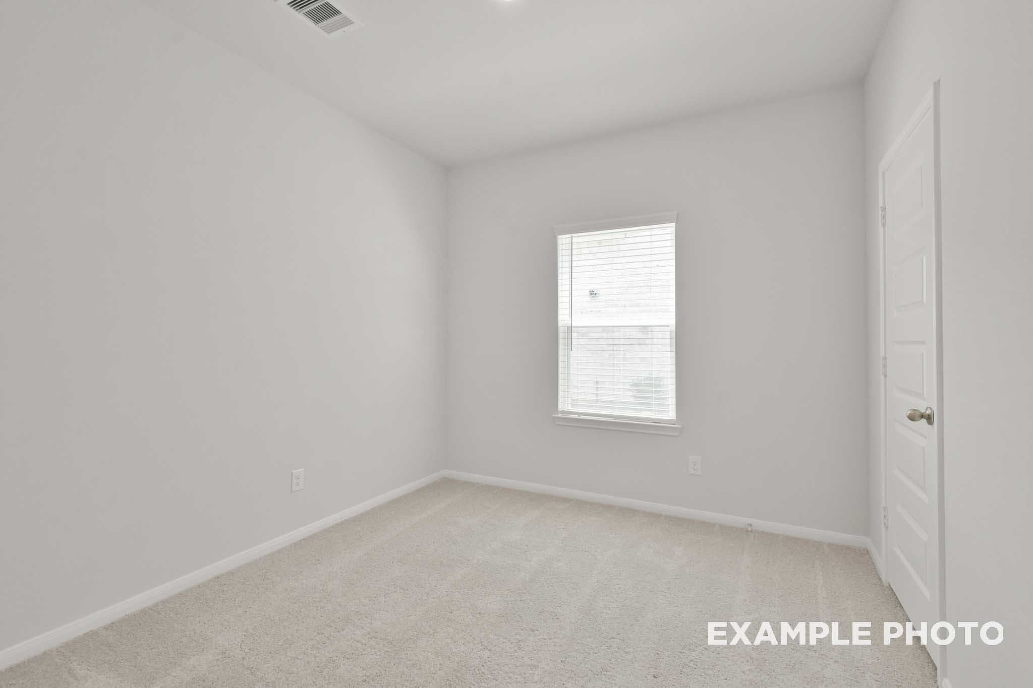 Spacious secondary bedroom in The Comal floor plan with neutral gray walls, carpet flooring, large window with blinds
