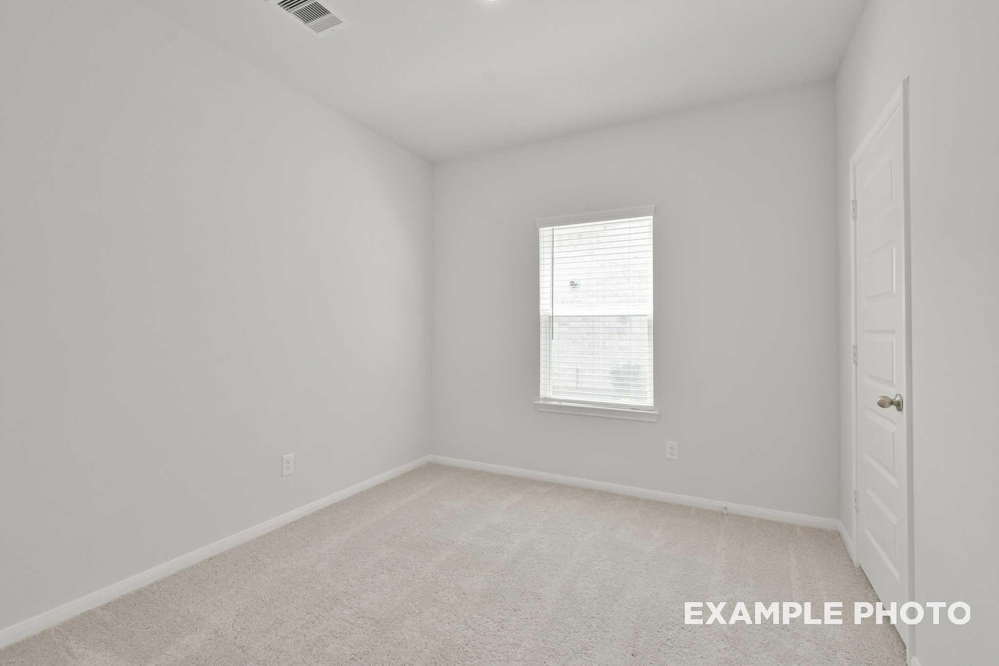 Spacious secondary bedroom in The Comal floor plan with neutral gray walls, carpet flooring, large window with blinds