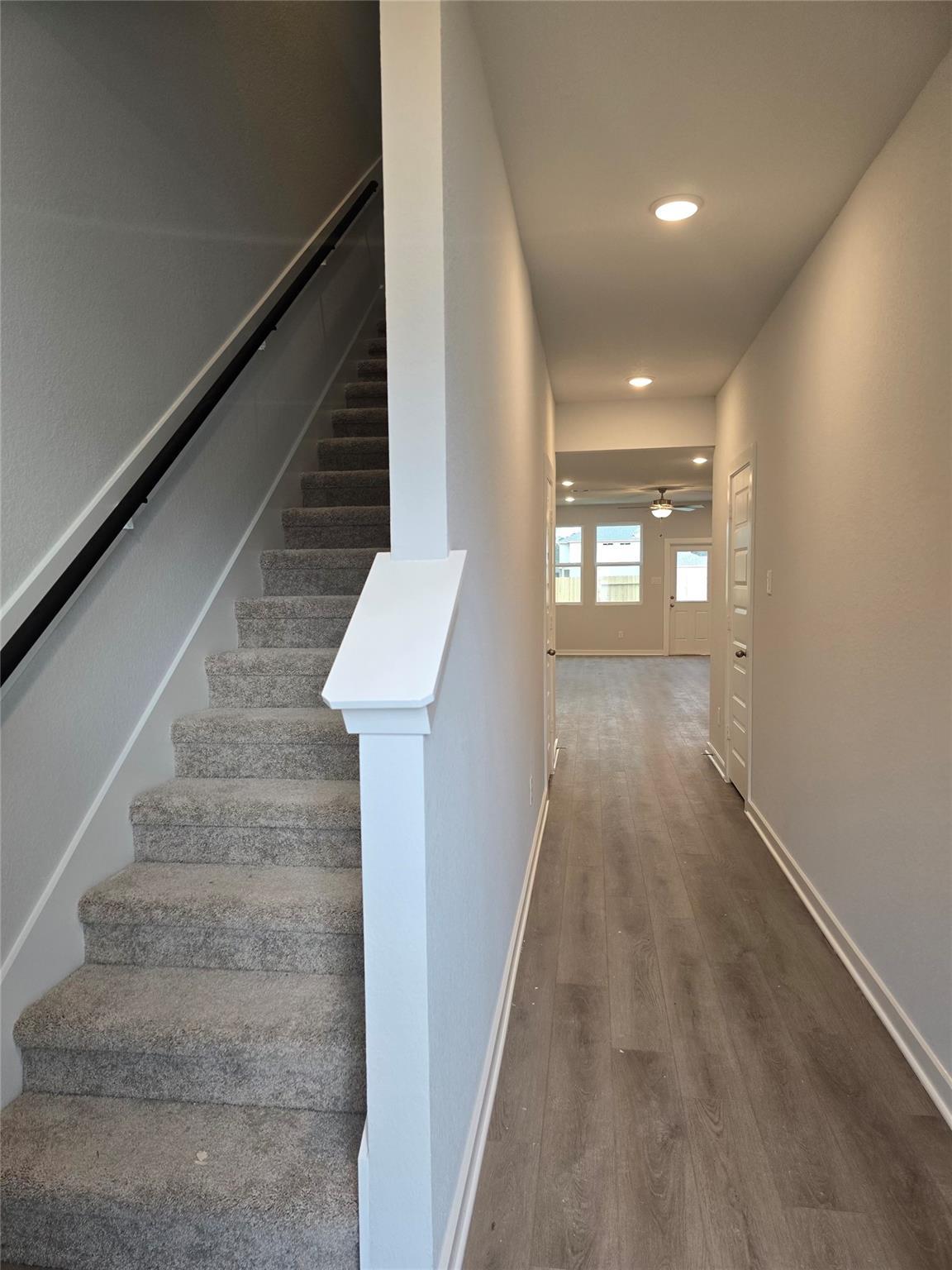 Carpeted staircase with white railing and wide hallway featuring luxury vinyl plank flooring in The Brazos E 5-bedroom home, Davidson Homes, Cleveland, Texas