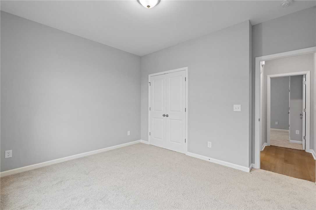 Spacious bedroom with light gray walls, beige carpet, and double white doors in Davidson Homes The Luna B, Opelika, Alabama