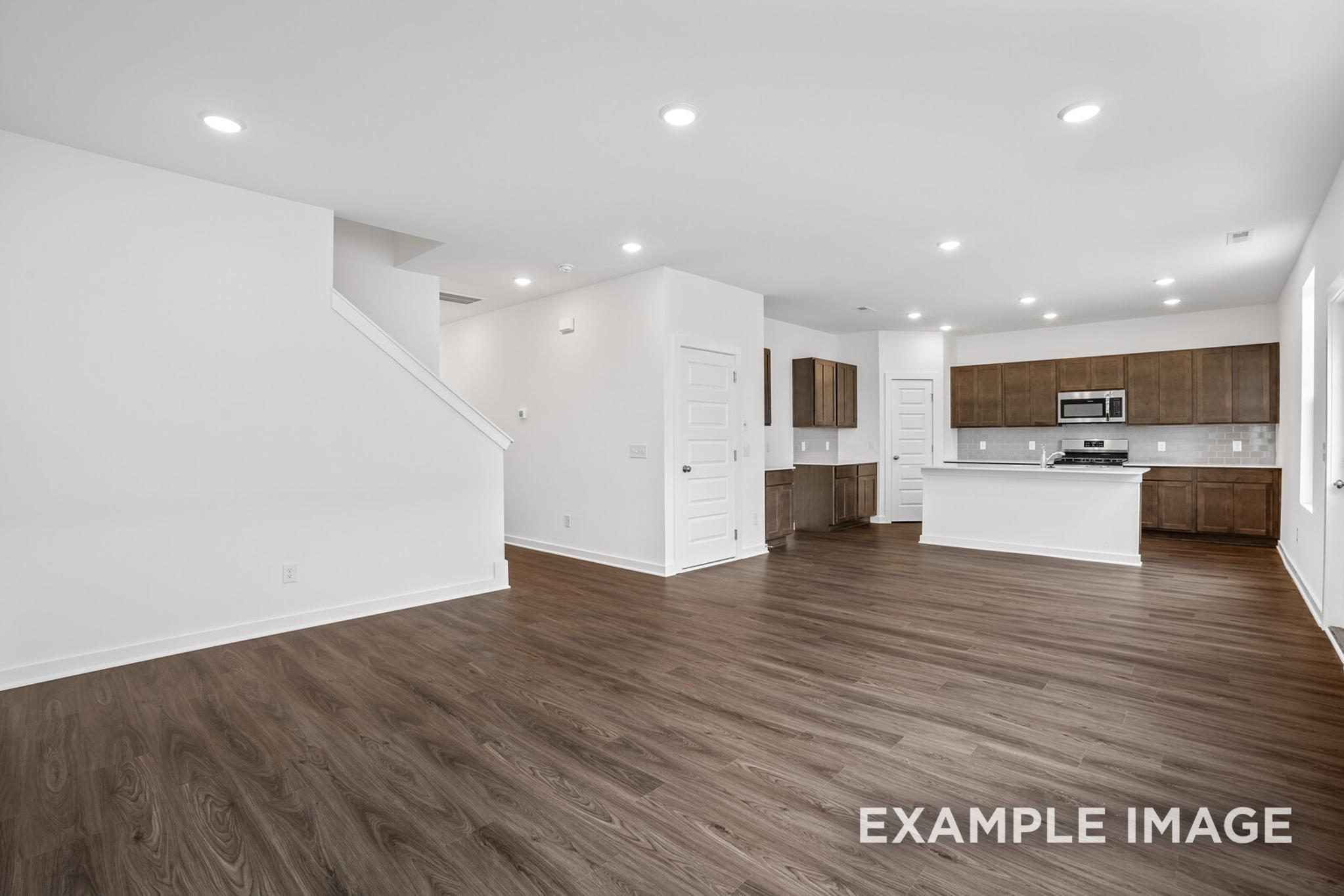 Spacious open-concept kitchen and living area in The Logan C home featuring white cabinetry, large island, hardwood floors, and staircase