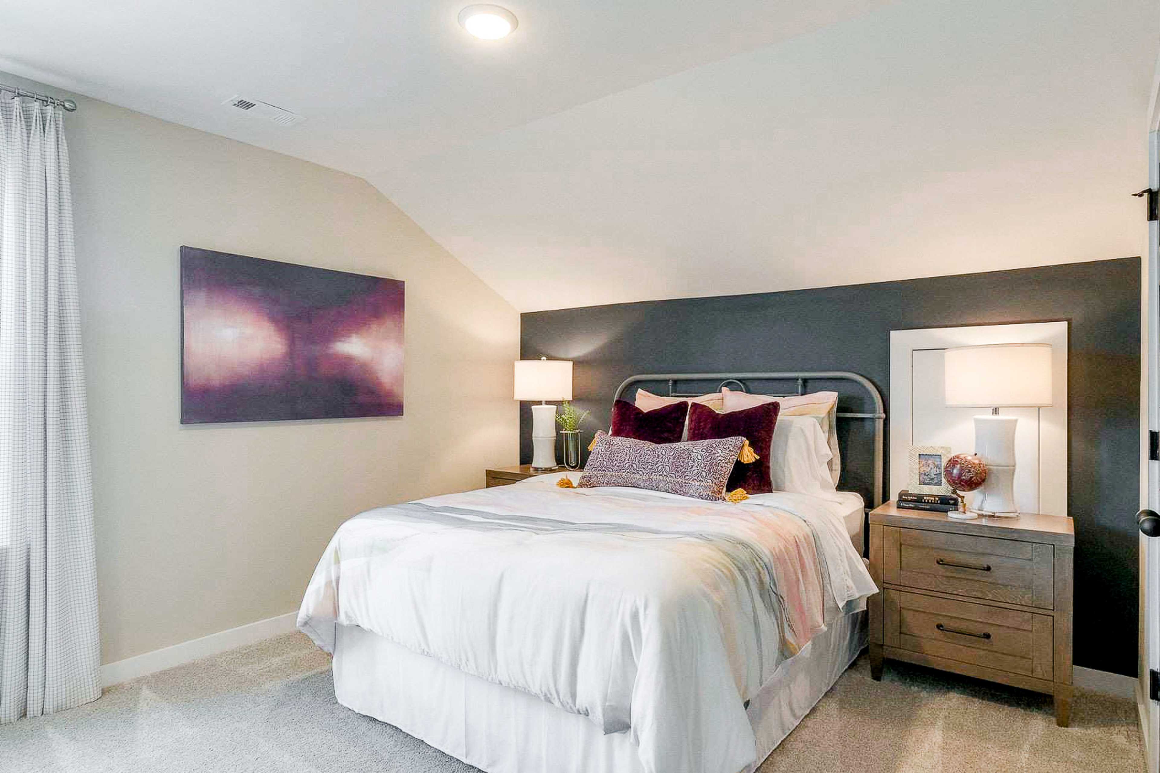 Cozy bedroom with white bed, plush pillows, abstract art, and gray accent wall at The Meadows in Smyrna TN by Davidson Homes