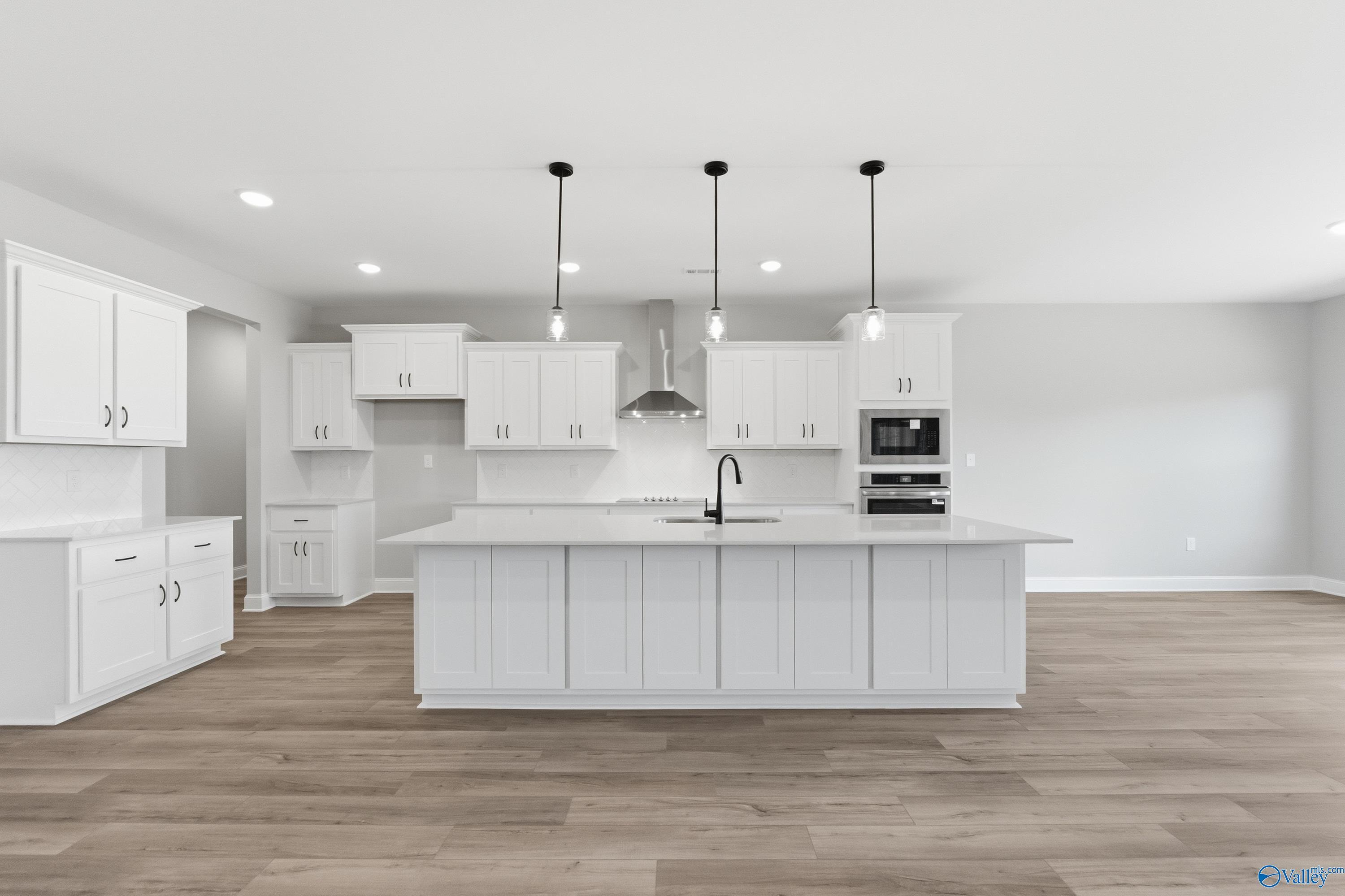 Modern white kitchen with large island, stainless appliances, and pendant lights in Davidson Homes The Finleigh, Meridianville, Alabama