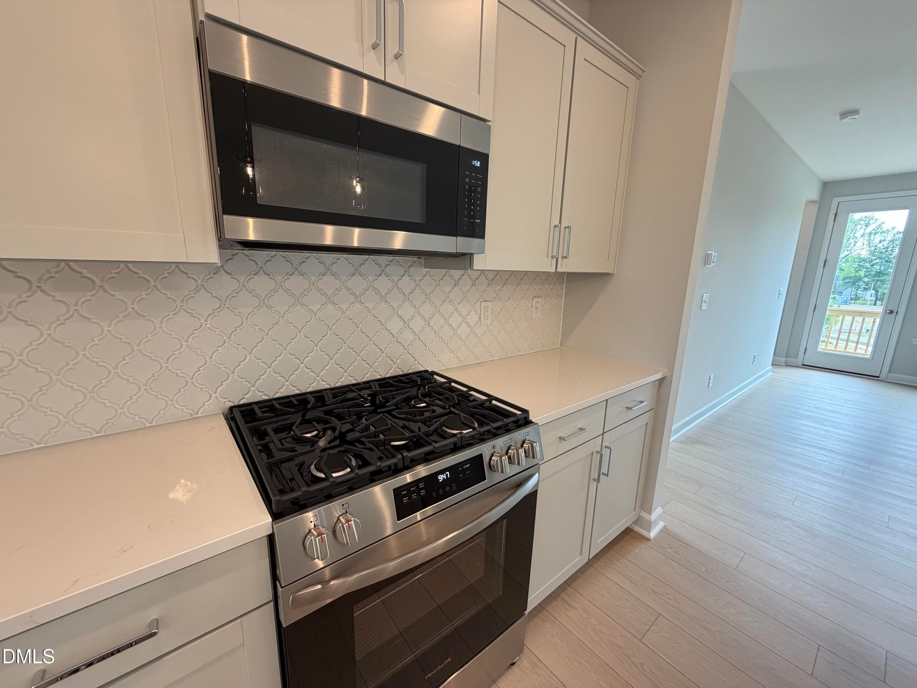 Modern kitchen featuring white shaker cabinets, quartz countertops, stainless Frigidaire gas range, and French doors to patio in Davidson Homes The Mitchell, Knightdale NC
