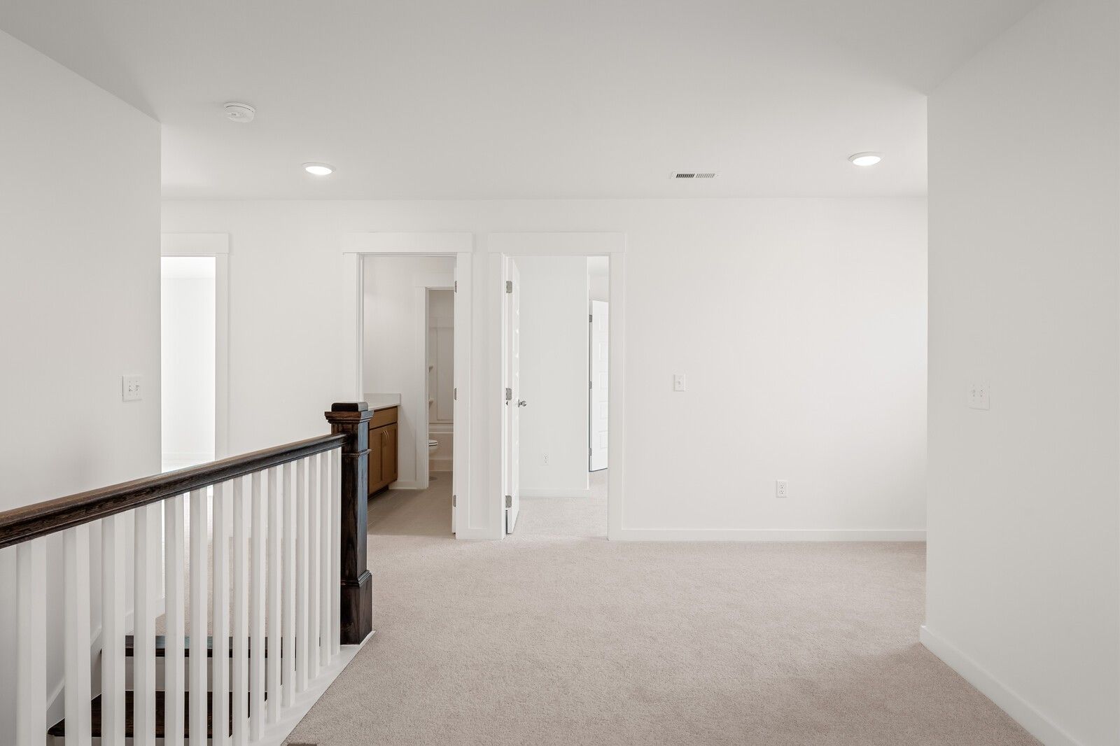 Bright upstairs hallway with white walls, beige carpet, wooden balustrade, and open bathroom in Davidson Homes The Ash C, Mt. Juliet