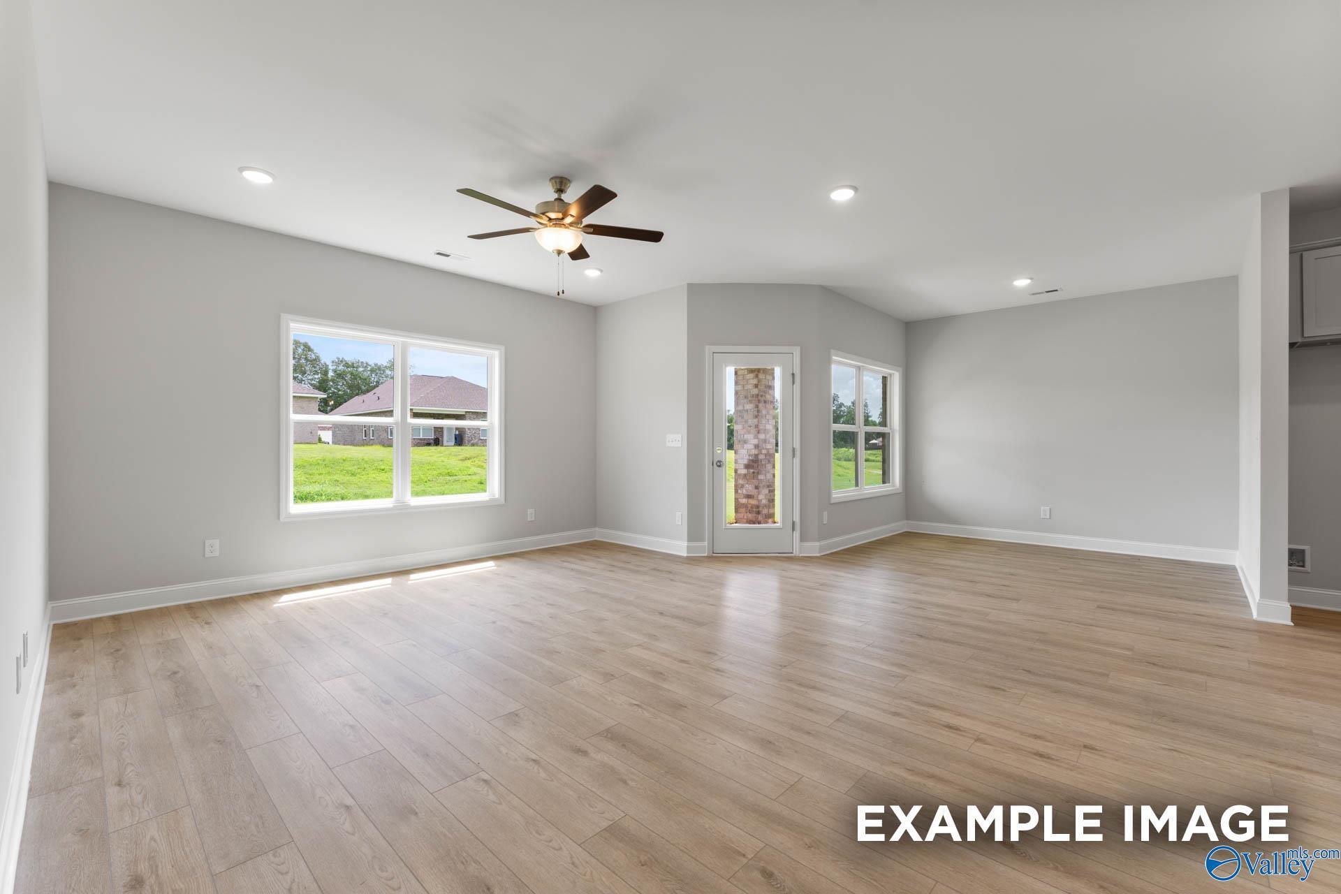 Bright open living room with hardwood floors, ceiling fan, and large windows to green yard in Davidson Homes The Daphne, Hazel Green