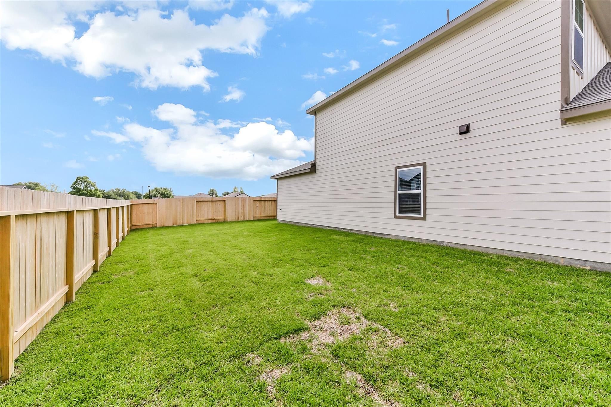 Fenced backyard with lush green lawn beside two-story Davidson Homes Sabine F in The Villages at WestPointe, Dayton, Texas