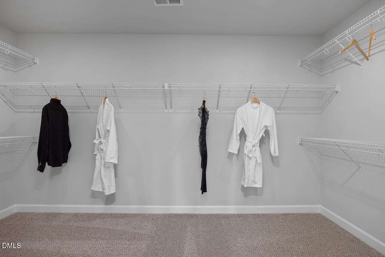 Spacious walk-in closet with wire shelving, hanging white robes and black dresses in Davidson Homes Hickory II C, Zebulon, NC