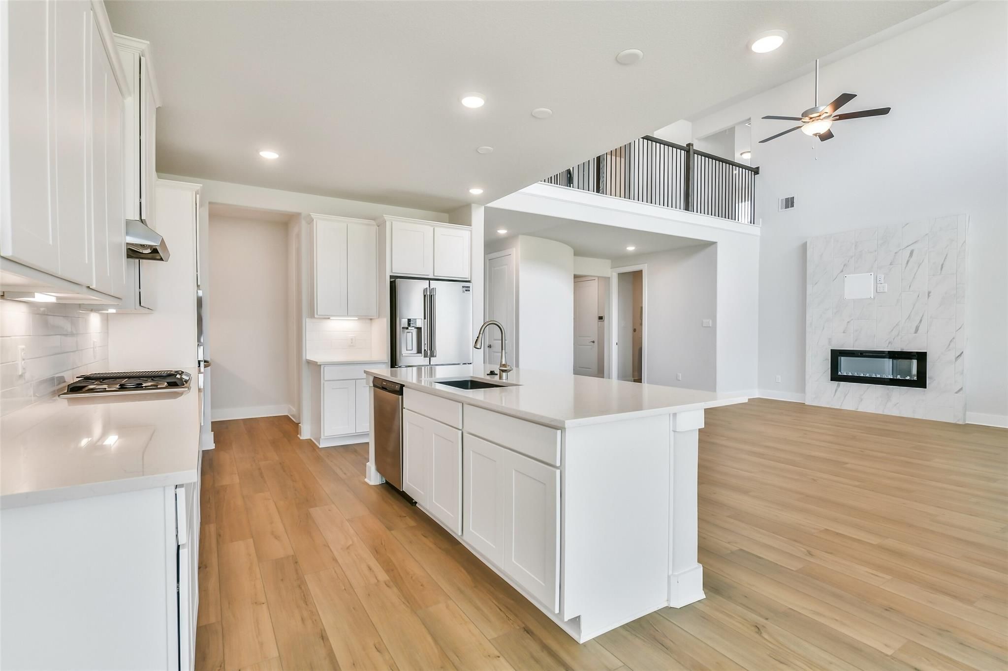 Modern open-concept kitchen with white cabinets, quartz island, stainless appliances, and fireplace in Davidson Homes The Victoria A, Lago Mar, Texas City