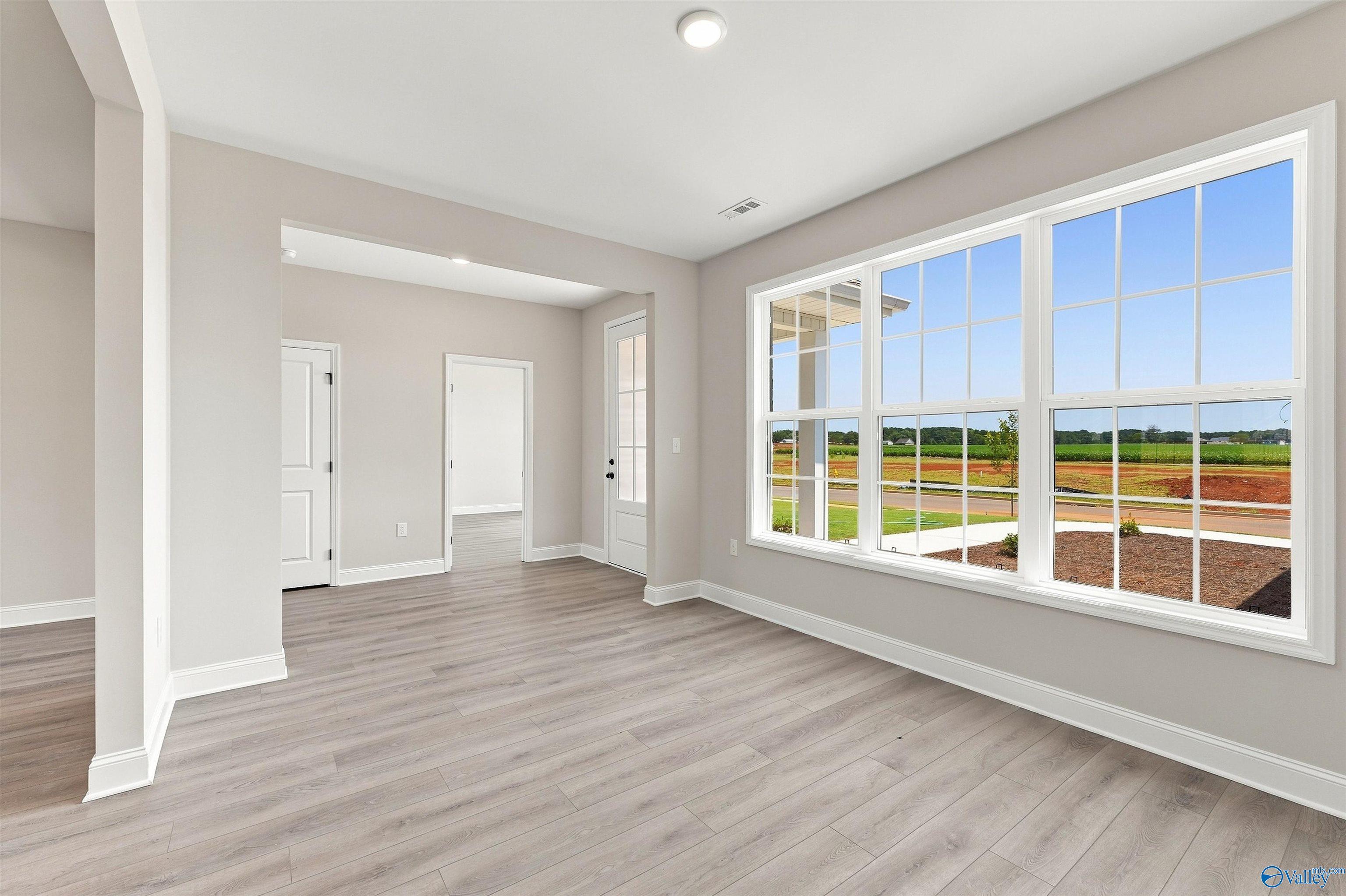 Bright living area with large windows and wood-look flooring in The Oxford floor plan at Kendall Farms, Toney, Alabama.
