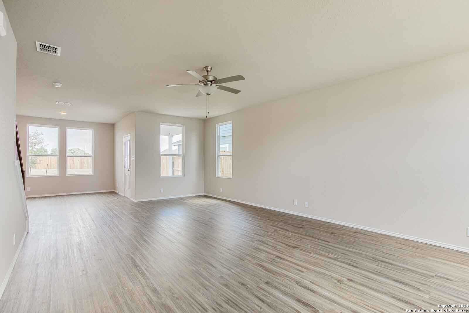 Spacious open living room with ceiling fan, light hardwood floors, and large windows in Davidson Homes The Murray H, Seguin, Texas