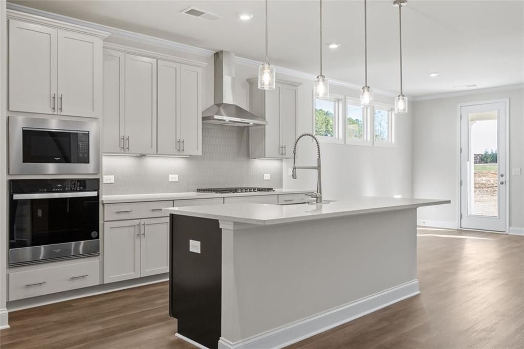 Modern kitchen featuring white shaker cabinets, stainless steel double oven, gas cooktop, and oversized island in Davidson Homes The Ash C at Wehunt Meadows, Hoschton, GA