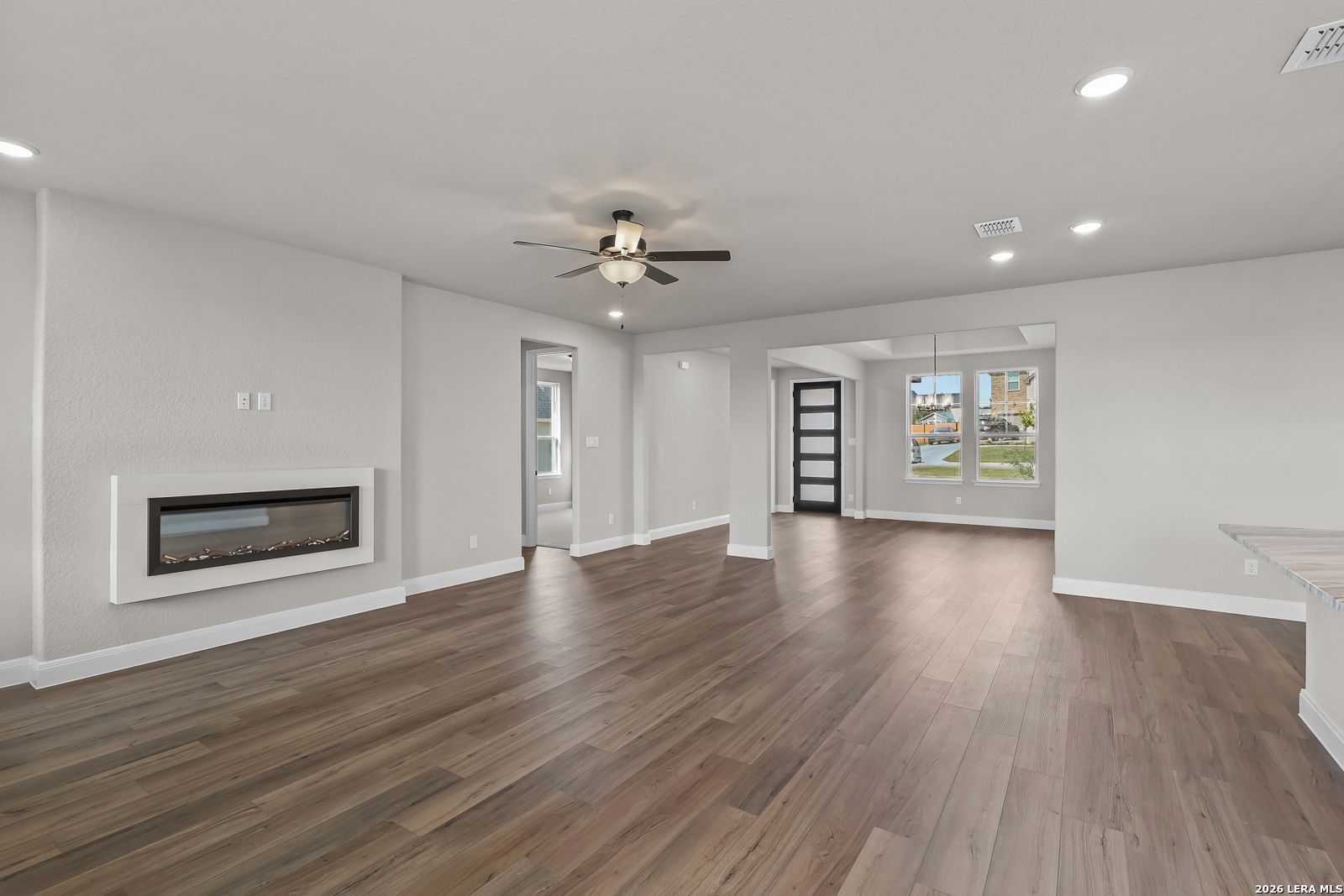 Open-concept living room with wood-look flooring, modern fireplace, and ceiling fan in Davidson Homes Foster E, Castroville, TX