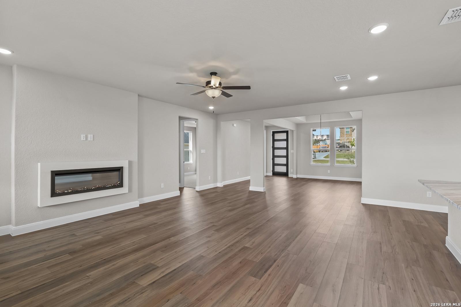 Open-concept living room with wood-look flooring, modern fireplace, and ceiling fan in Davidson Homes Foster E, Castroville, TX