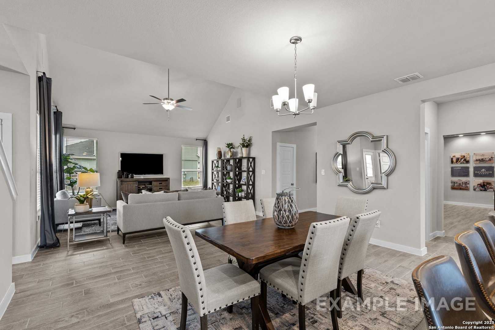 Open-concept living dining room with wood table, gray sofa, TV, and chandelier in The Collin B by Davidson Homes, Seguin, Texas