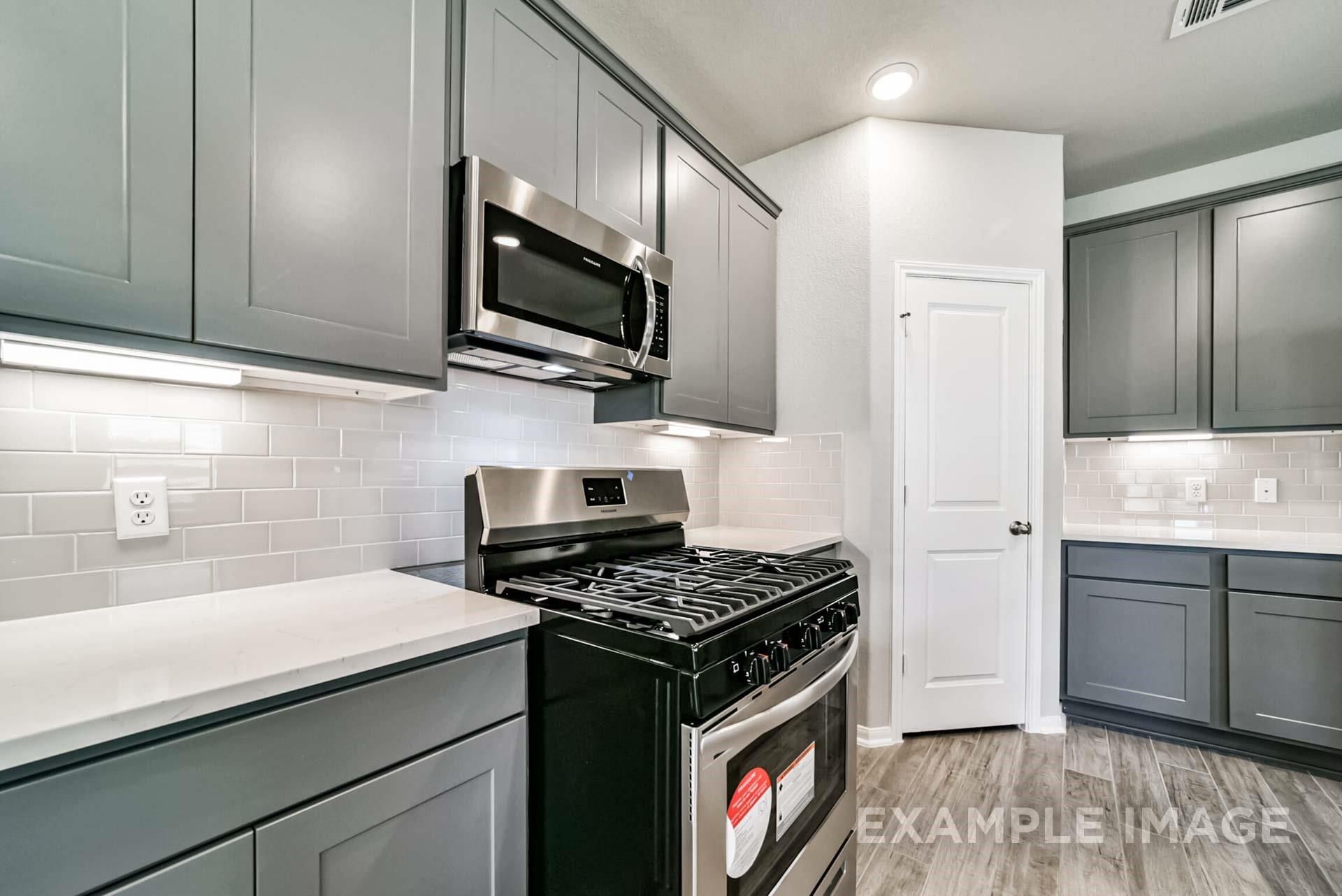 Modern kitchen with gray cabinets, subway tile backsplash, and stainless steel appliances in The Riviera A, Emberly, Texas.