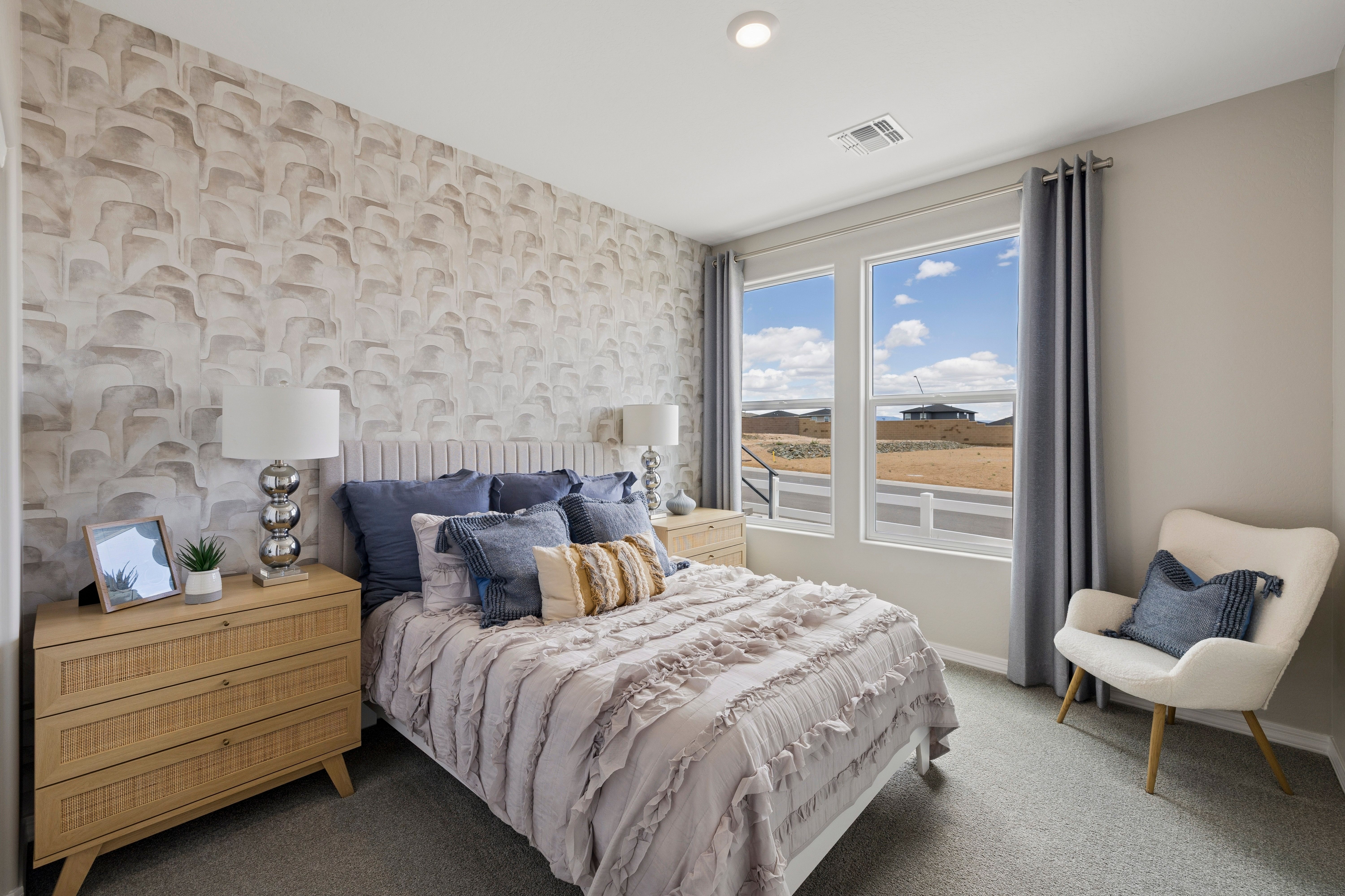 Cozy master bedroom at South Ranch in Prescott AZ with textured wallpaper, ruffled neutral bedding, woven dresser, and desert view window