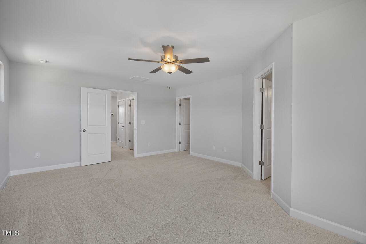 Spacious upstairs hallway with beige carpet, ceiling fan, and white bedroom doors in Davidson Homes The Graham plan, Fuquay-Varina, NC