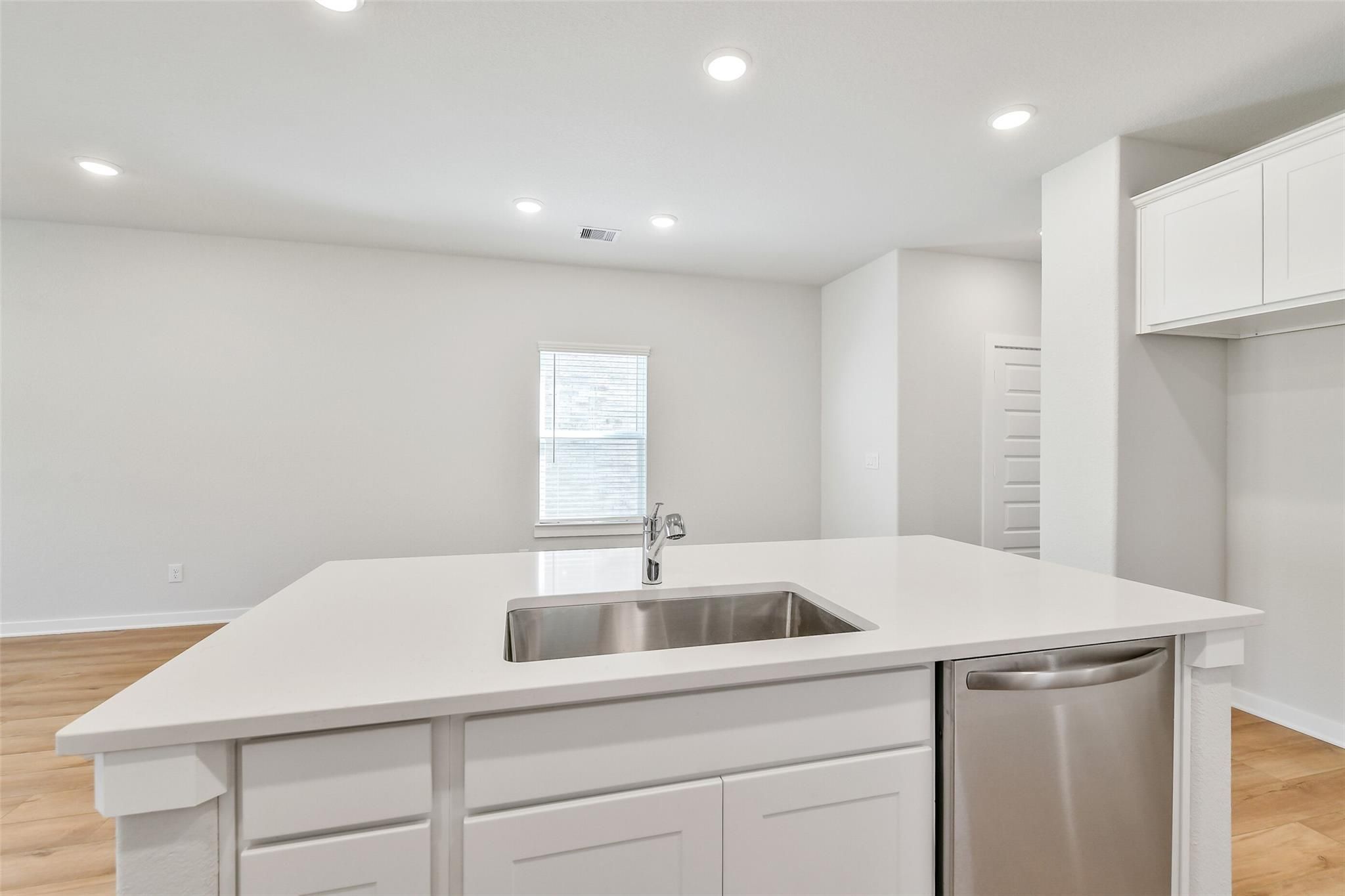 Spacious white kitchen island with stainless sink and dishwasher in Davidson Homes The Blanco E, Magnolia, Texas