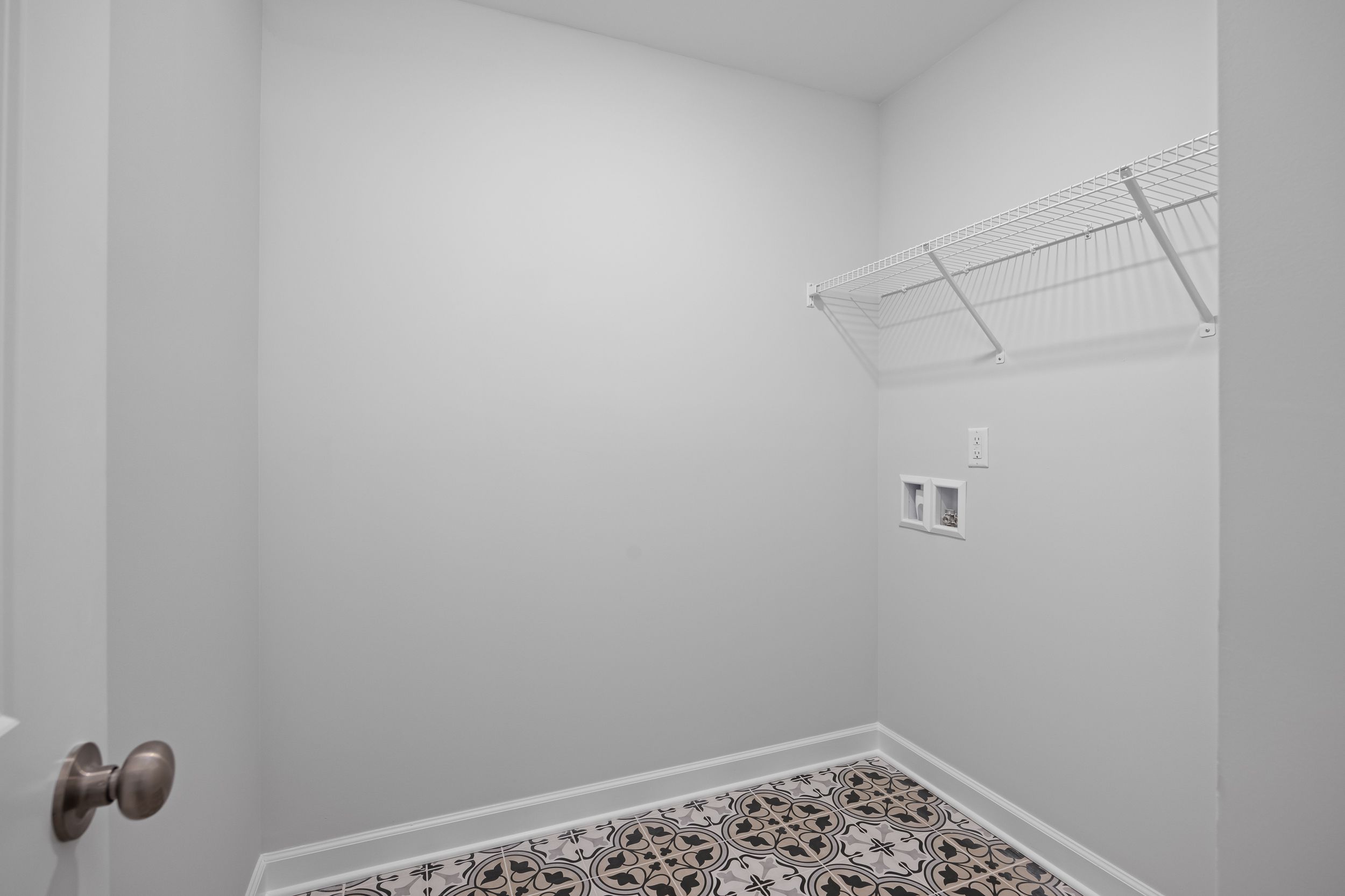 Laundry room in The Warren featuring patterned tile flooring, white walls, and convenient built-in wire shelving.