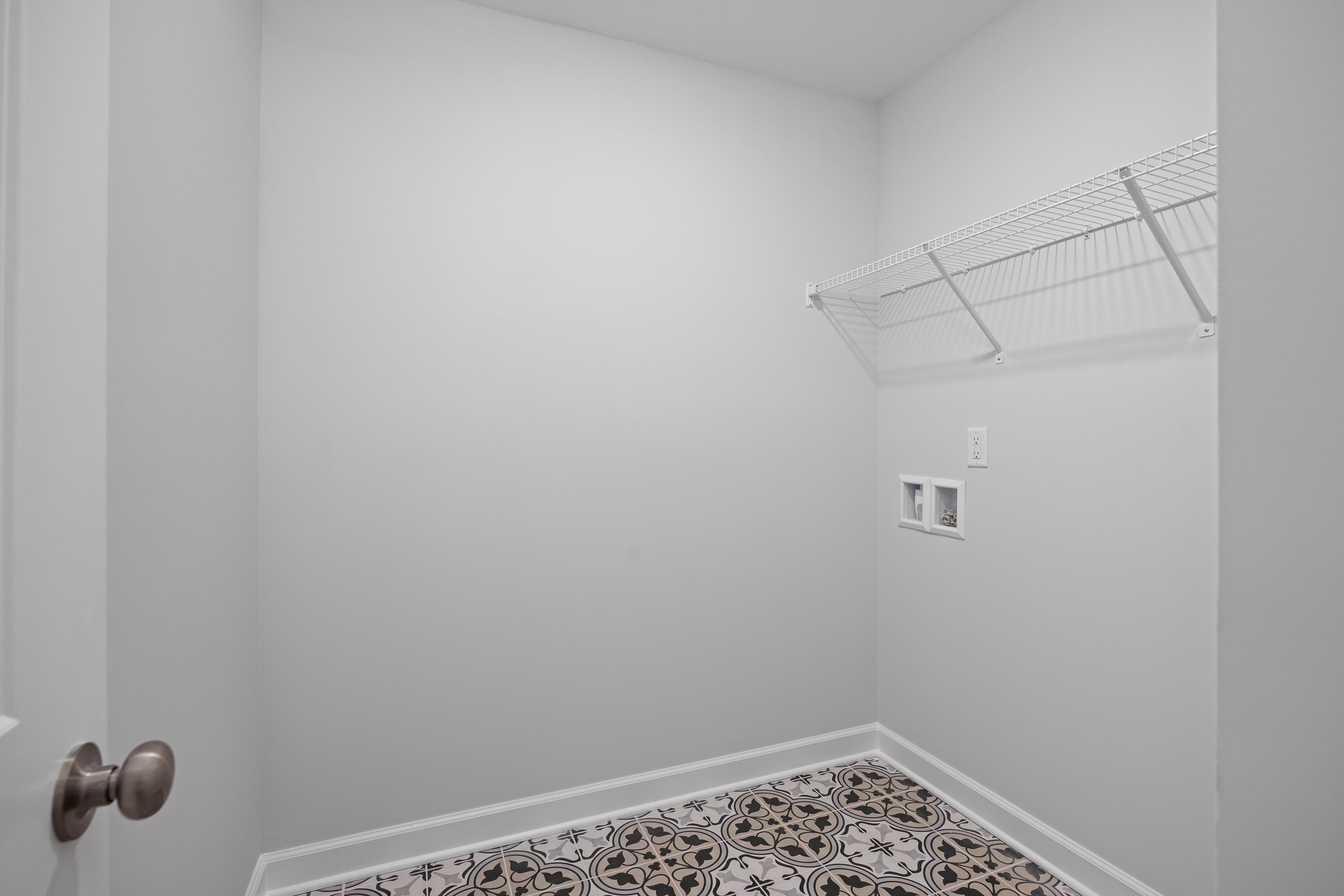 Laundry room in The Warren featuring patterned tile flooring, white walls, and convenient built-in wire shelving.