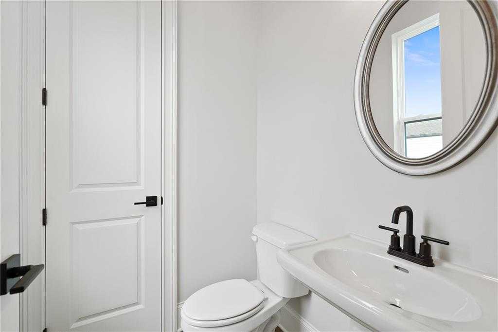 Elegant powder room with white pedestal sink, round mirror, toilet in Davidson Homes Seaside B, Woodstock, GA