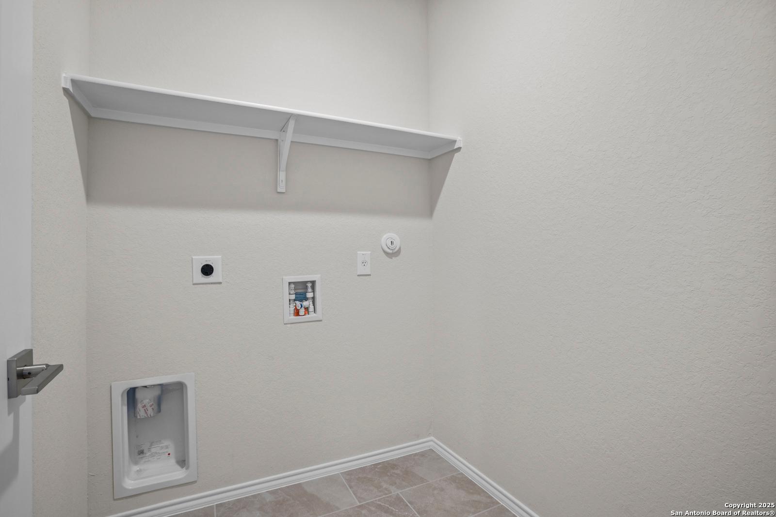Modern laundry room with utility sink, washer/dryer hookups, and built-in shelves in The Asheville J by Davidson Homes, San Antonio