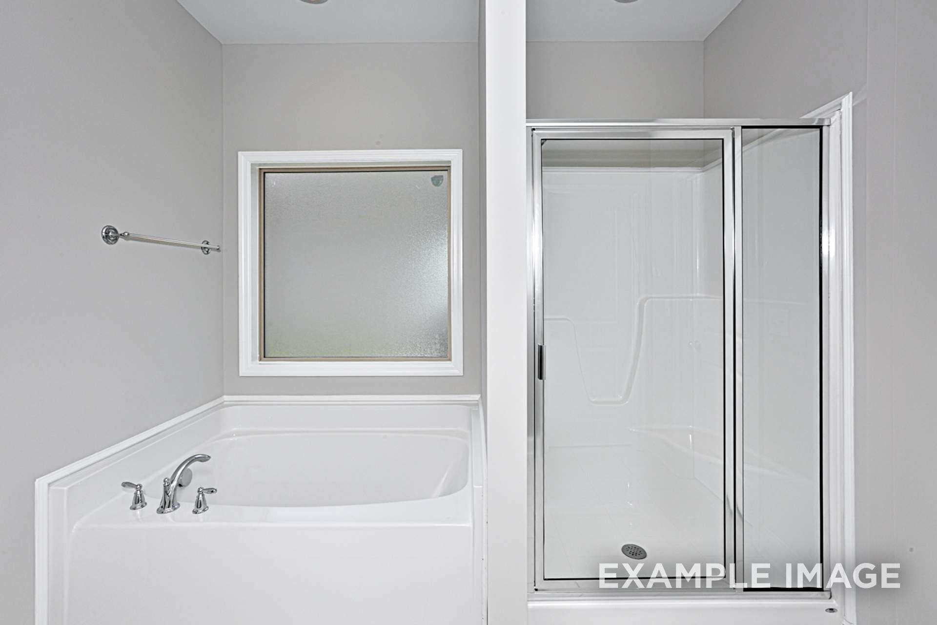 Spacious master bath in The Montgomery B with white soaking tub, glass shower doors, and frameless mirror