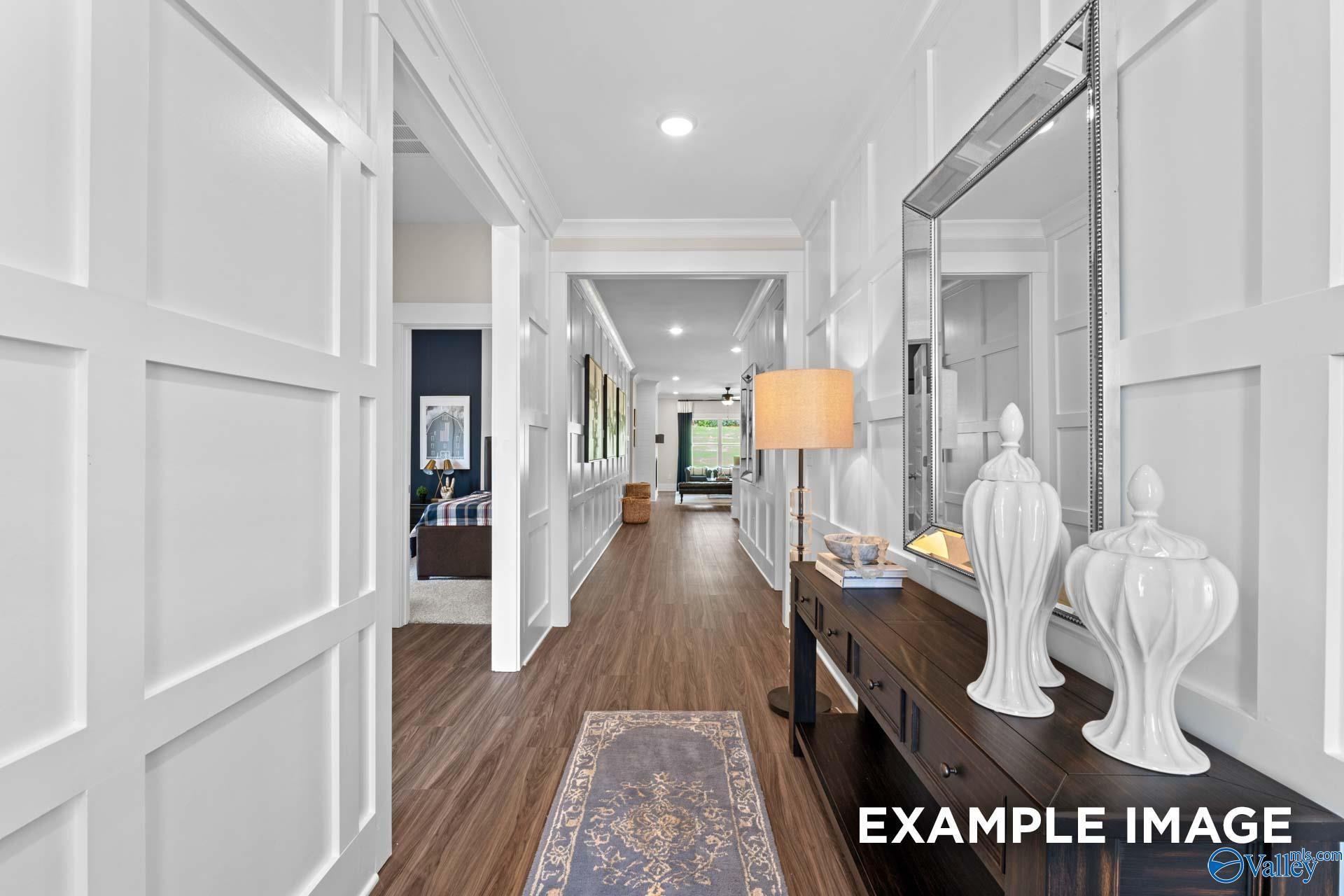 Elegant hallway with white paneled walls, hardwood floors, floor lamp, and decorative vases in Davidson Homes The Daphne F, New Market, Alabama