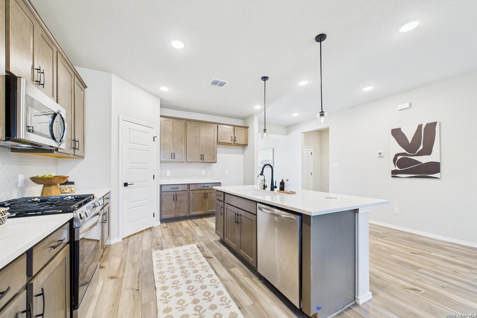 Modern kitchen featuring white shaker cabinets, quartz island with sink, stainless appliances, and hardwood floors in Davidson Homes The Douglas E, San Antonio