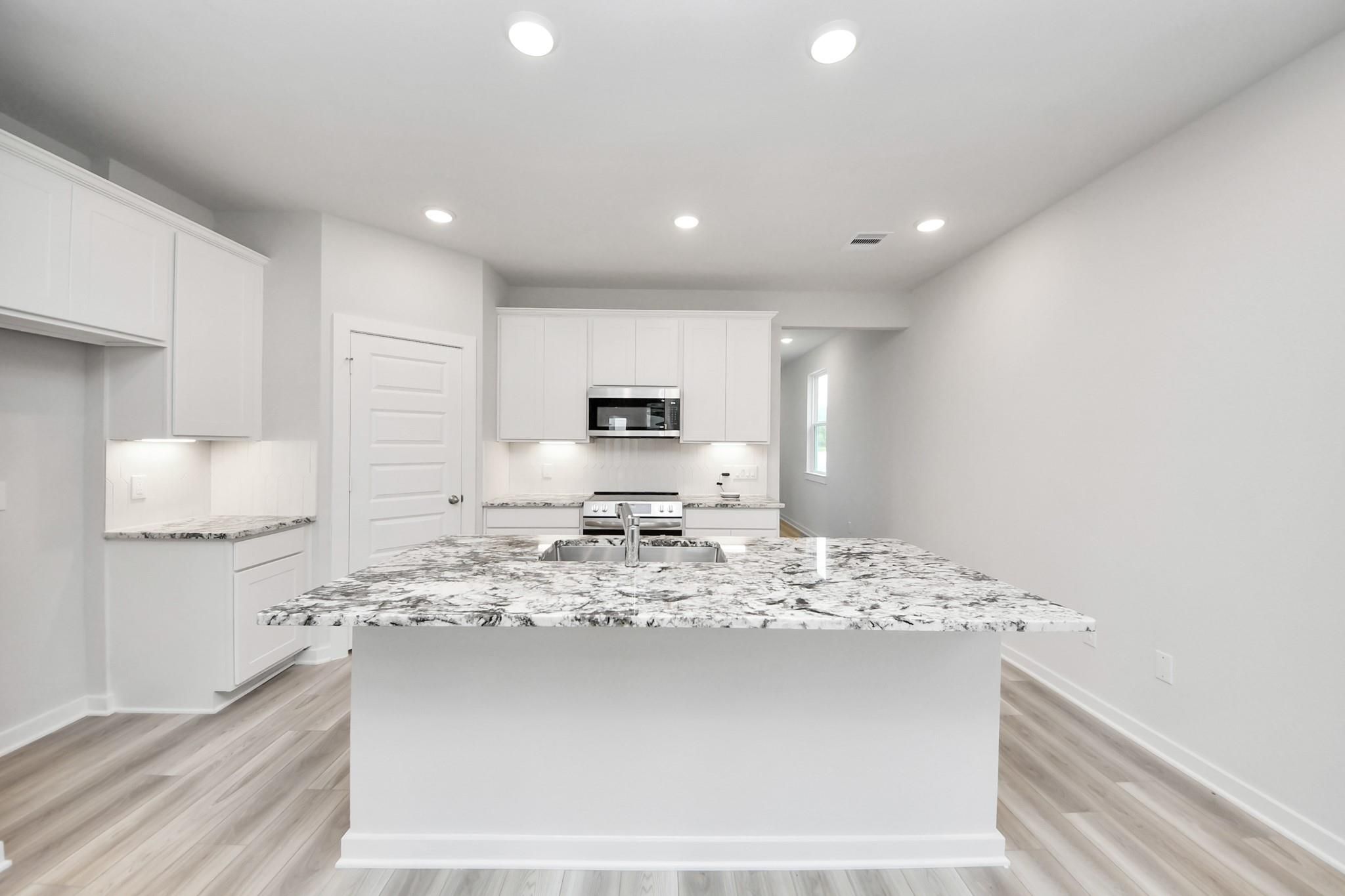 Modern kitchen with granite island and white cabinets in The Sabine F floor plan at Liberty Estates, Cleveland, Texas.