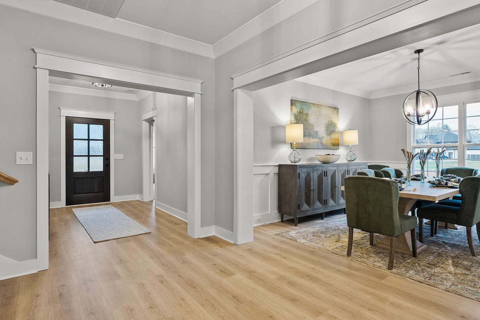 Spacious dining room in The Oxford home with elegant credenza, chandelier, upholstered chairs, and open entryway
