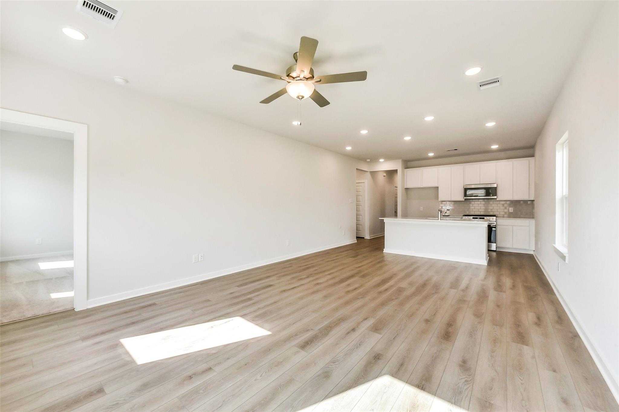 Bright open-concept living and kitchen with luxury vinyl plank floors, ceiling fan, and white island in Davidson Homes Comal G, Dayton TX