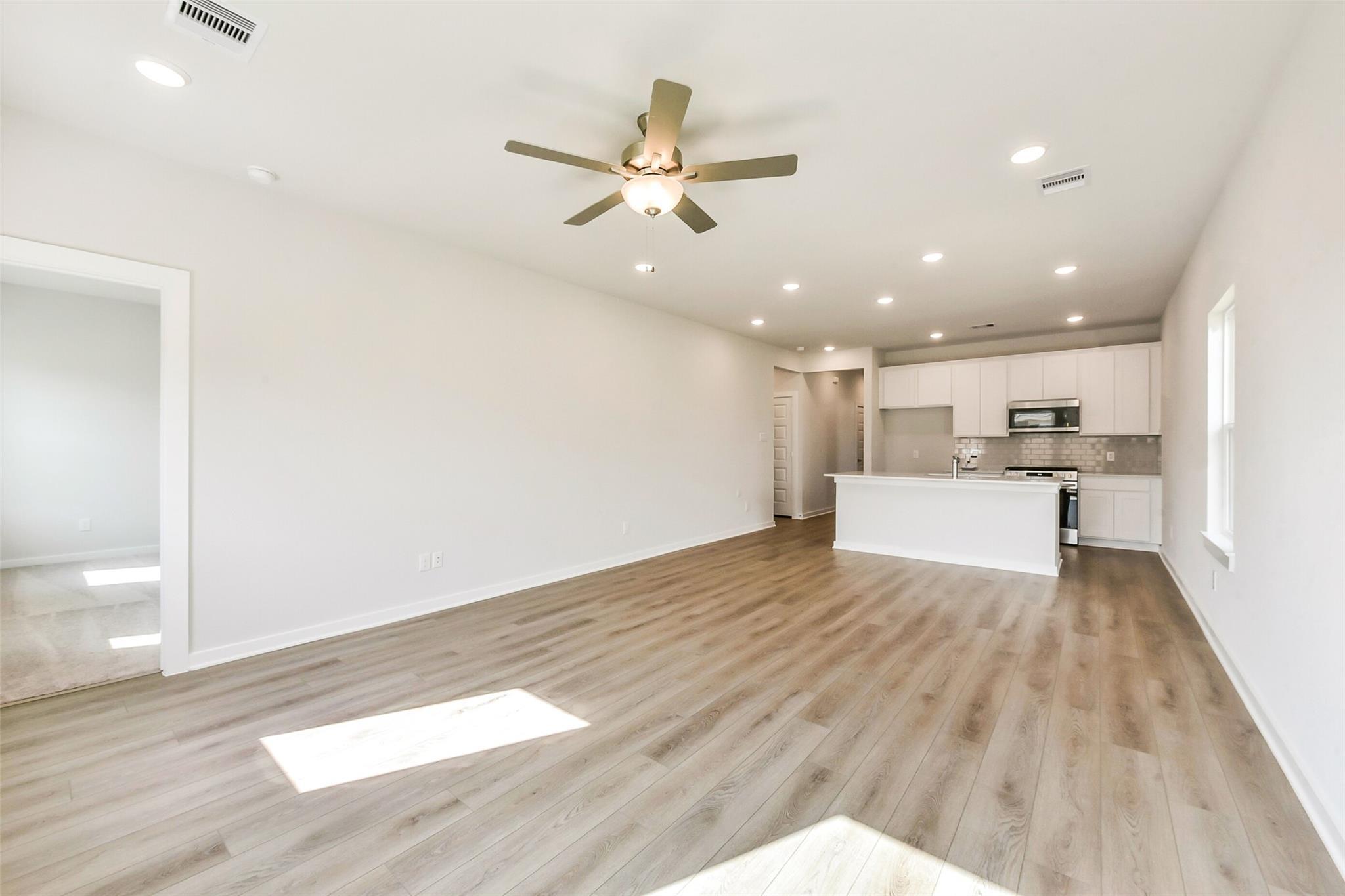 Open-concept living and kitchen area with ceiling fan, laminate wood floors, white cabinets, stainless appliances in 3-bedroom Davidson Homes The Comal G, Dayton Texas