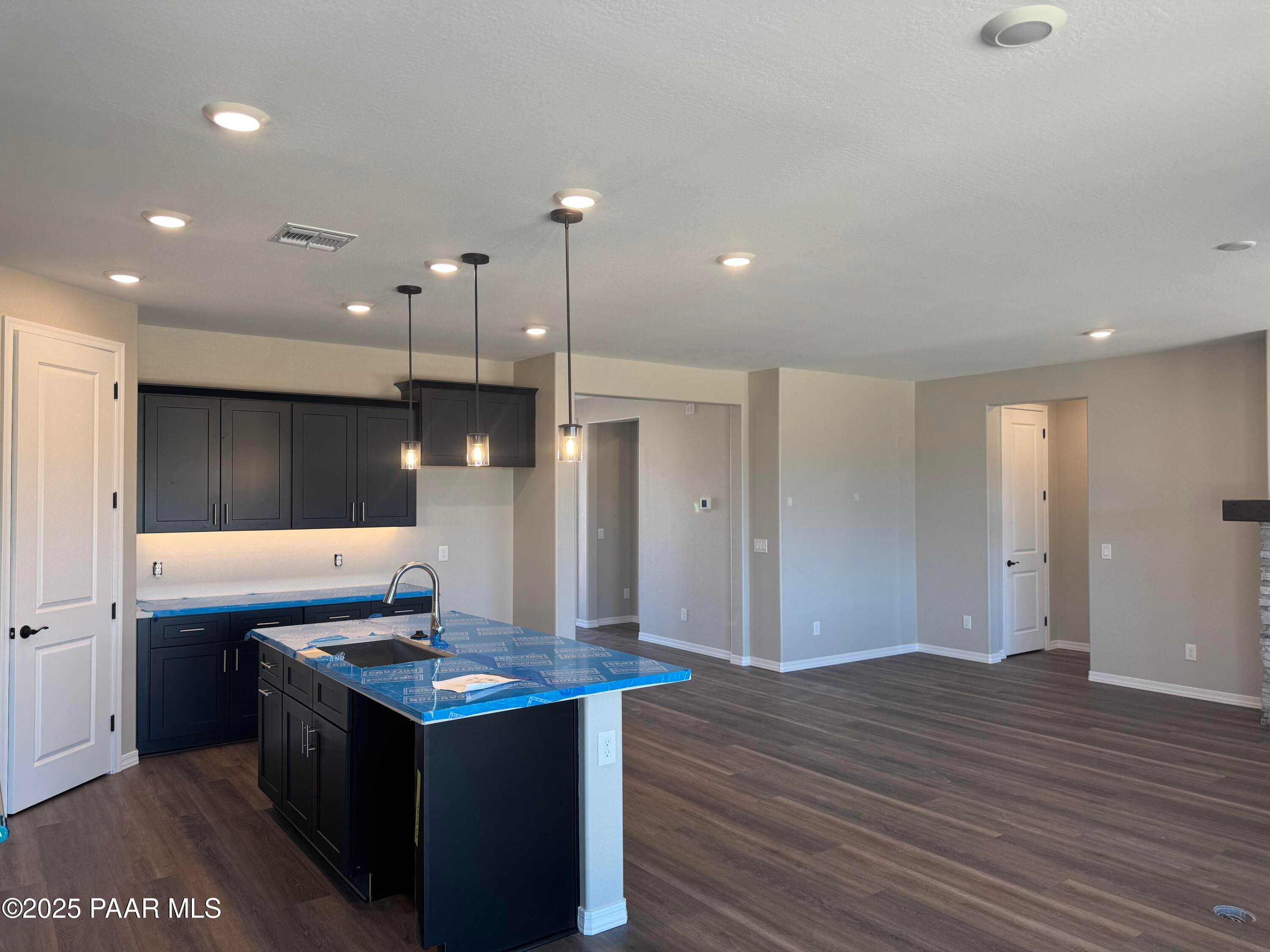 Modern open kitchen with dark cabinets, central island sink, pendant lights, and hardwood floors in Davidson Homes The Durango II A, Prescott, Arizona