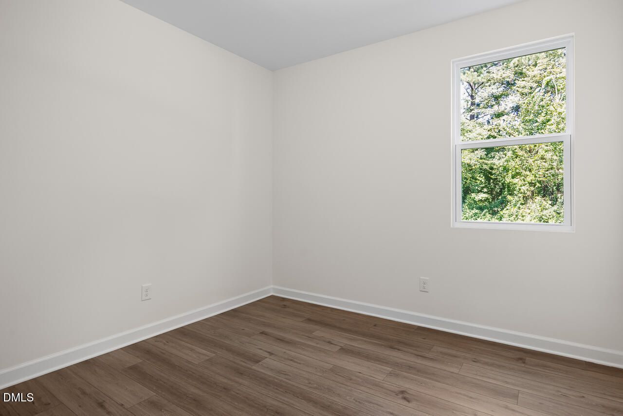 Bright empty bedroom with hardwood-style flooring and window view of trees in Davidson Homes The Willow B, Zebulon, NC
