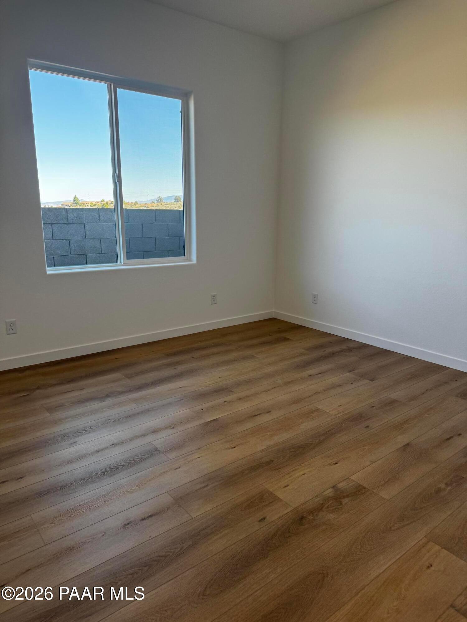 Sunny bedroom with large window overlooking block wall and blue sky, white walls, light oak LVP flooring in The Blaze C, Prescott AZ