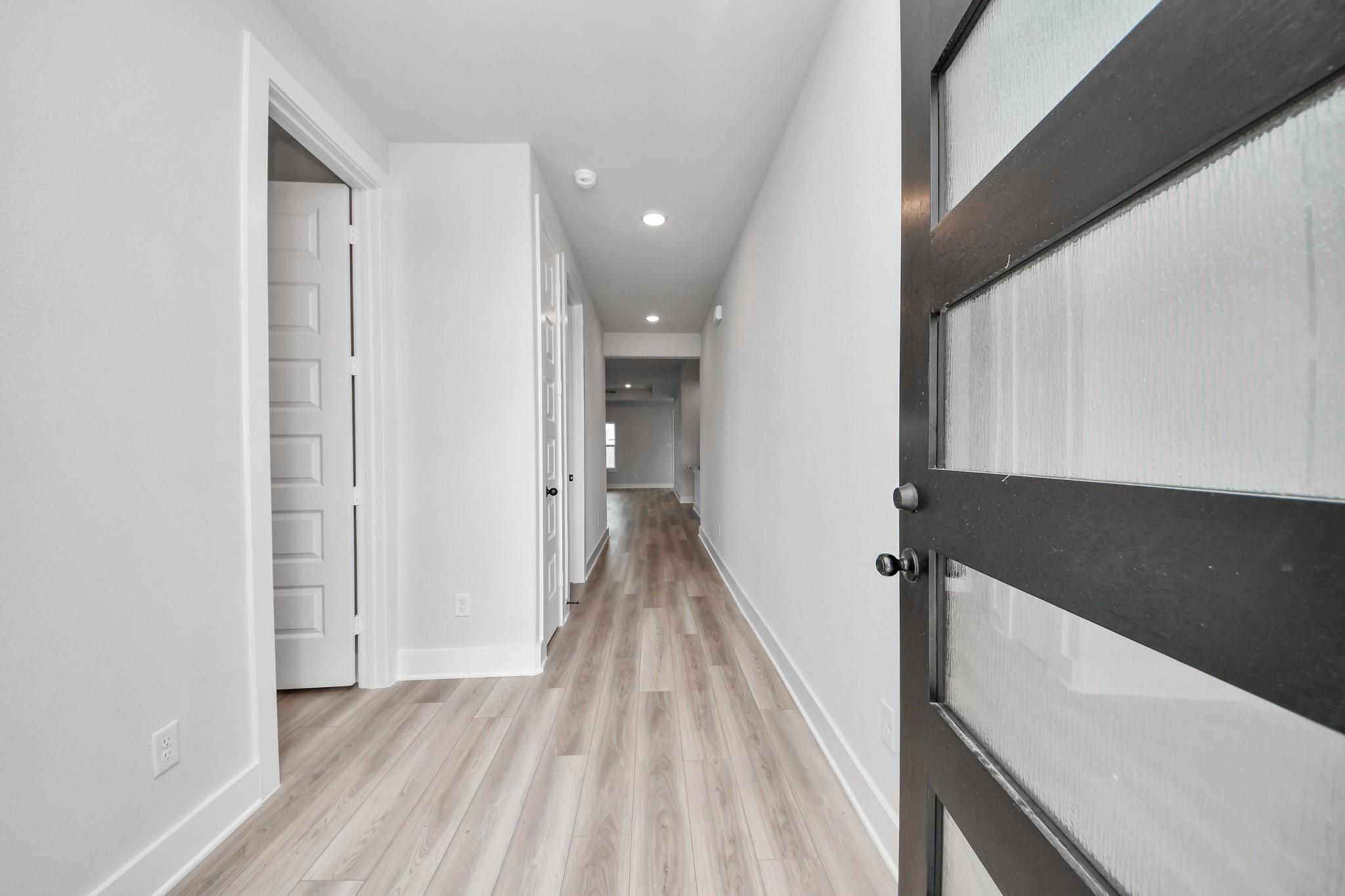 Bright hallway with wood-look flooring and modern glass-paneled door in Laguna C floor plan, Sunterra, Katy, Texas.