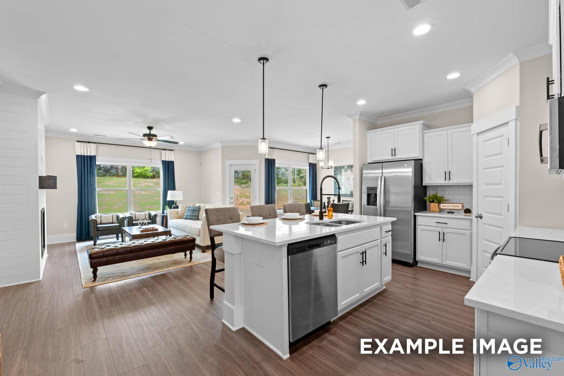 Open-concept kitchen and living room with white cabinets, stainless appliances, island, and fireplace in Davidson Homes The Daphne F, New Market, Alabama