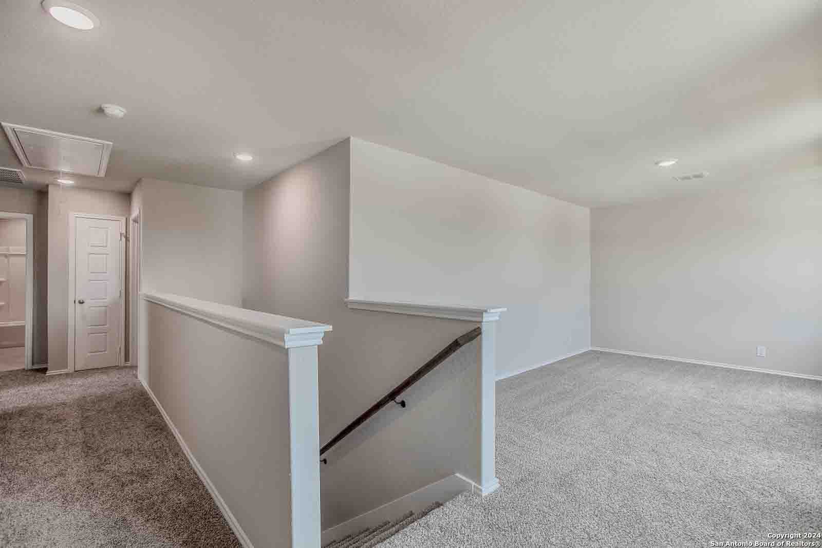 Carpeted upstairs hallway with wooden stair railing and bedroom doors in The Murray H 4-bedroom home, Hannah Heights, Seguin, Texas